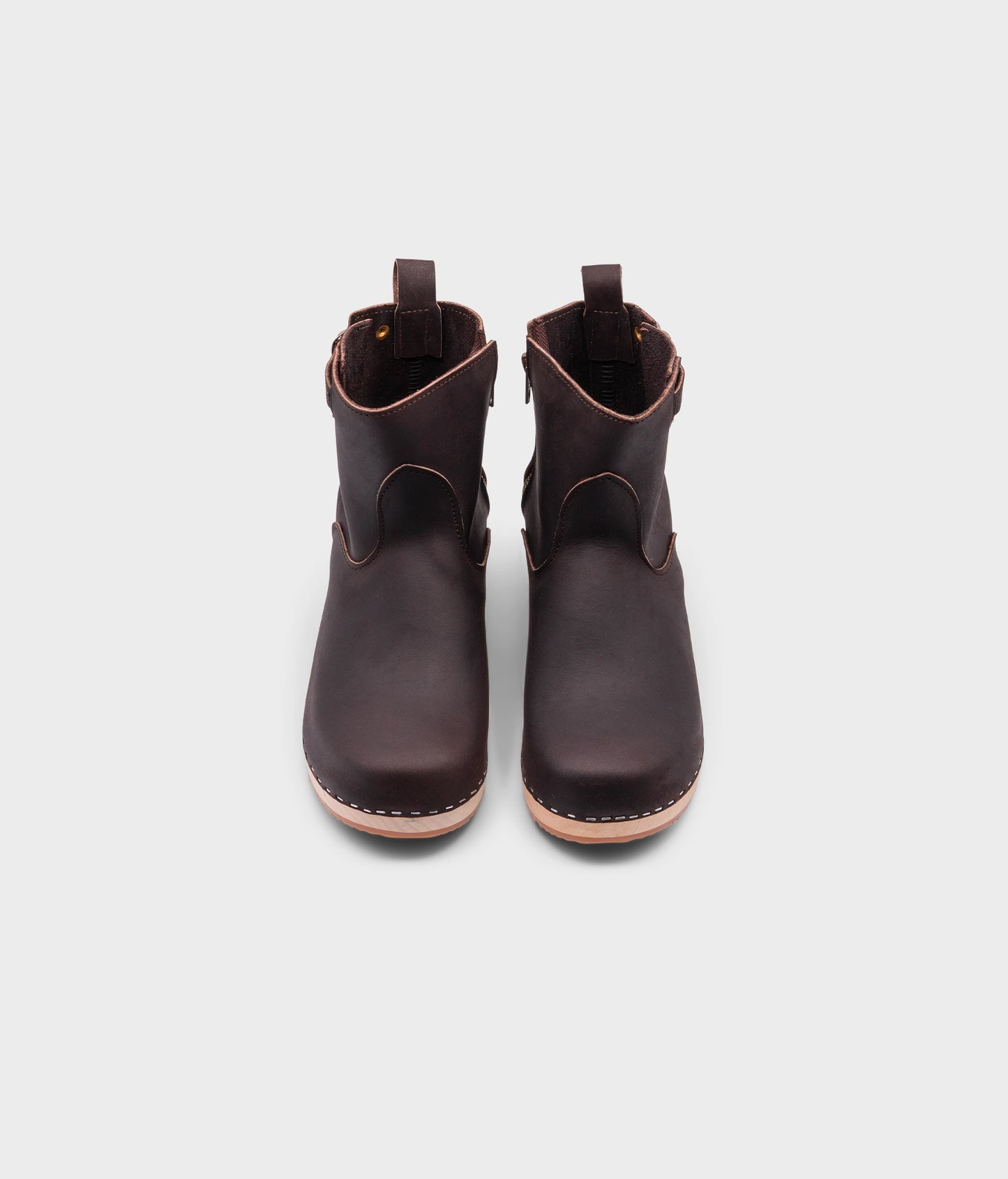 low-heeled clog boots in dark brown leather stapled on a light wooden base