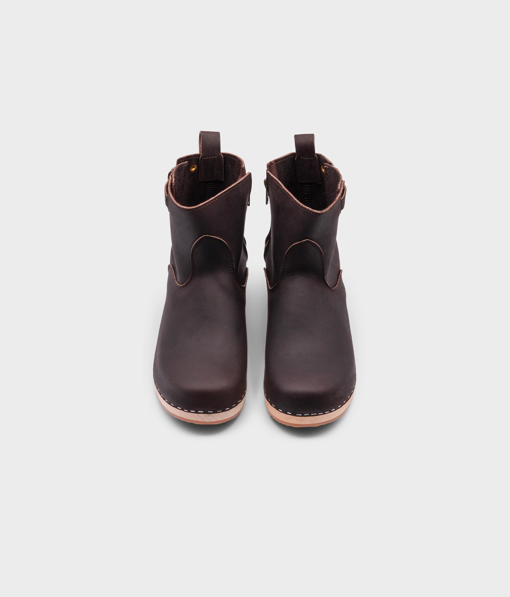 low-heeled clog boots in dark brown leather stapled on a light wooden base