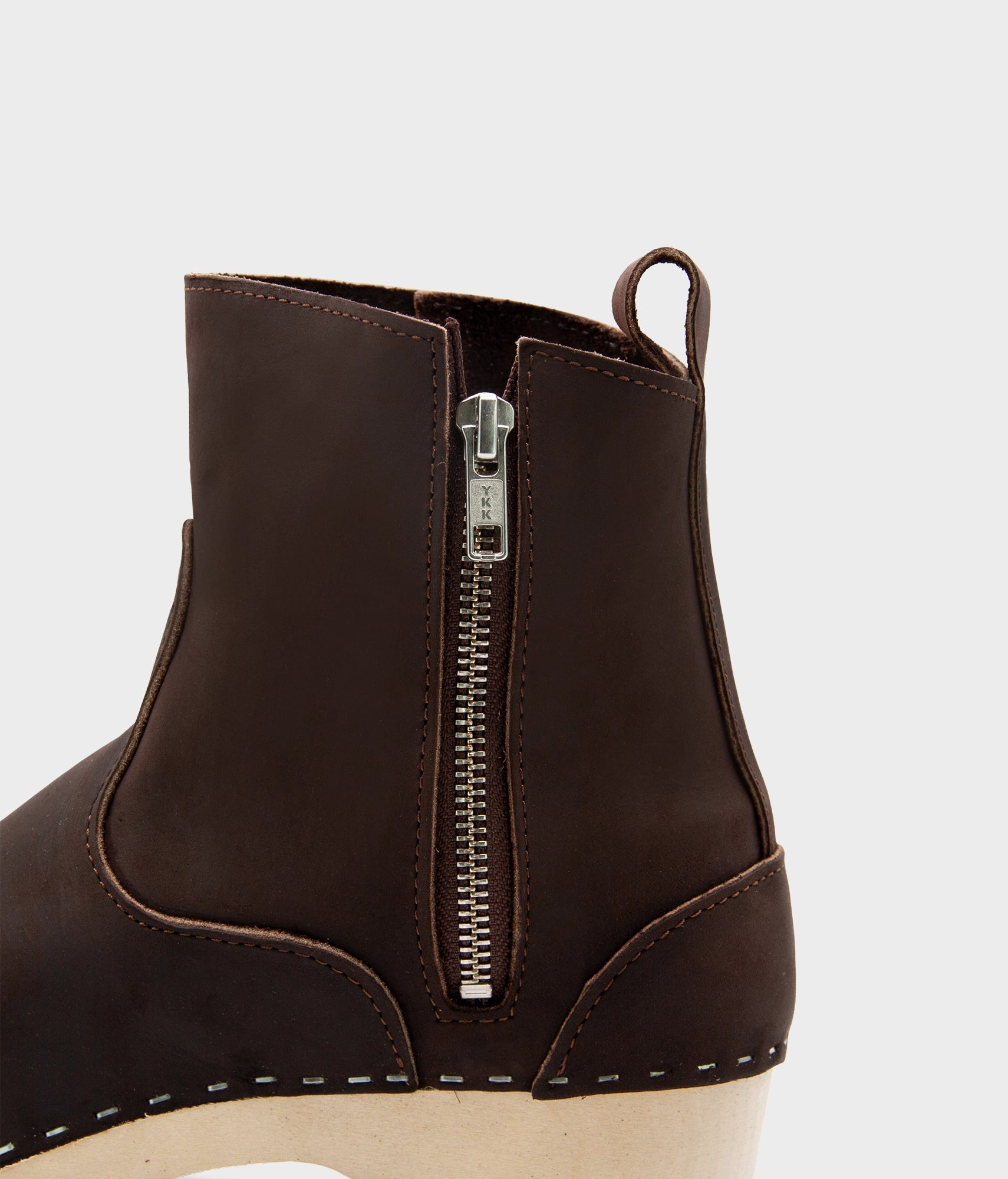 low-heeled clog boots in dark brown leather stapled on a light wooden base