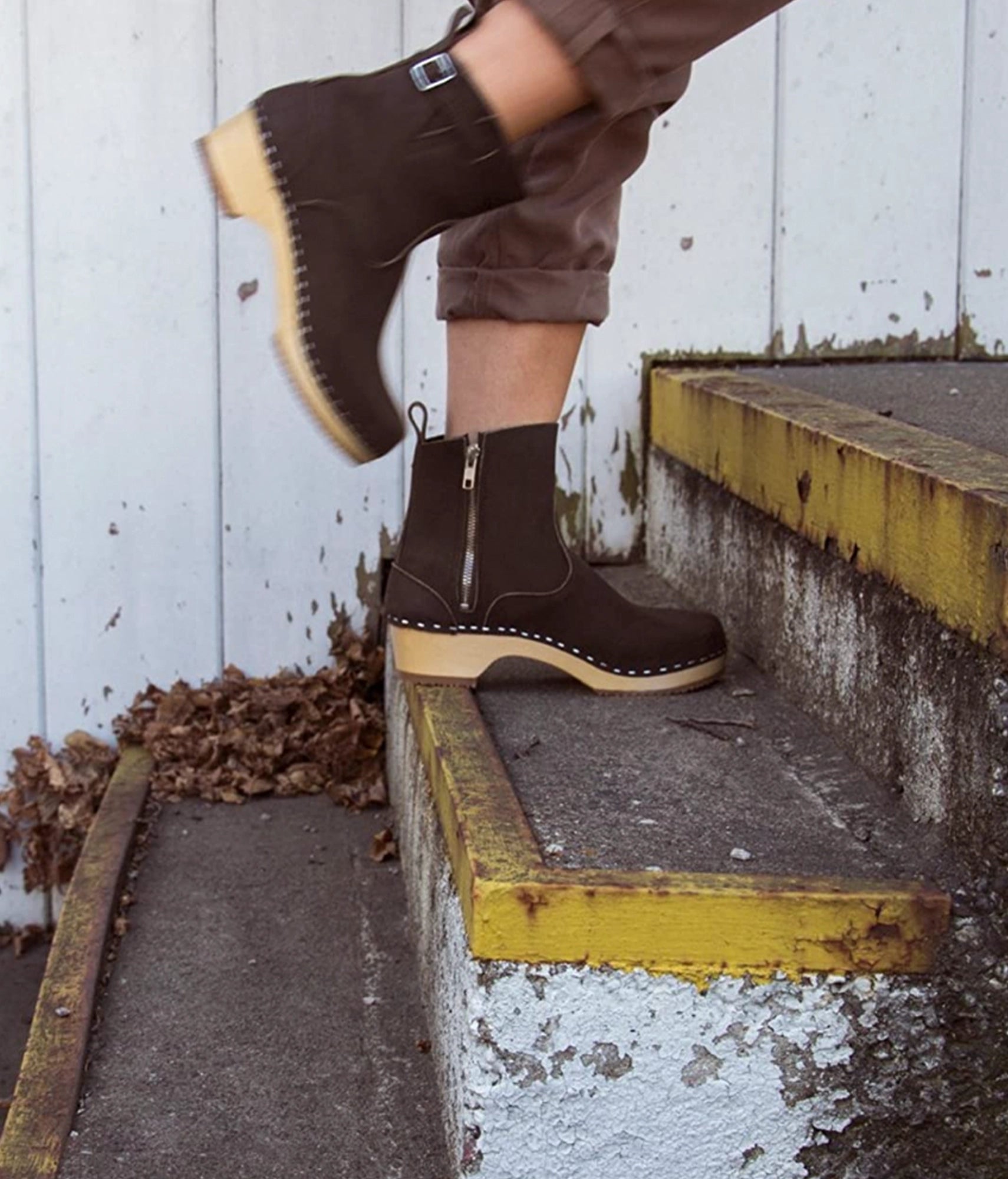 low-heeled clog boots in dark brown leather stapled on a light wooden base