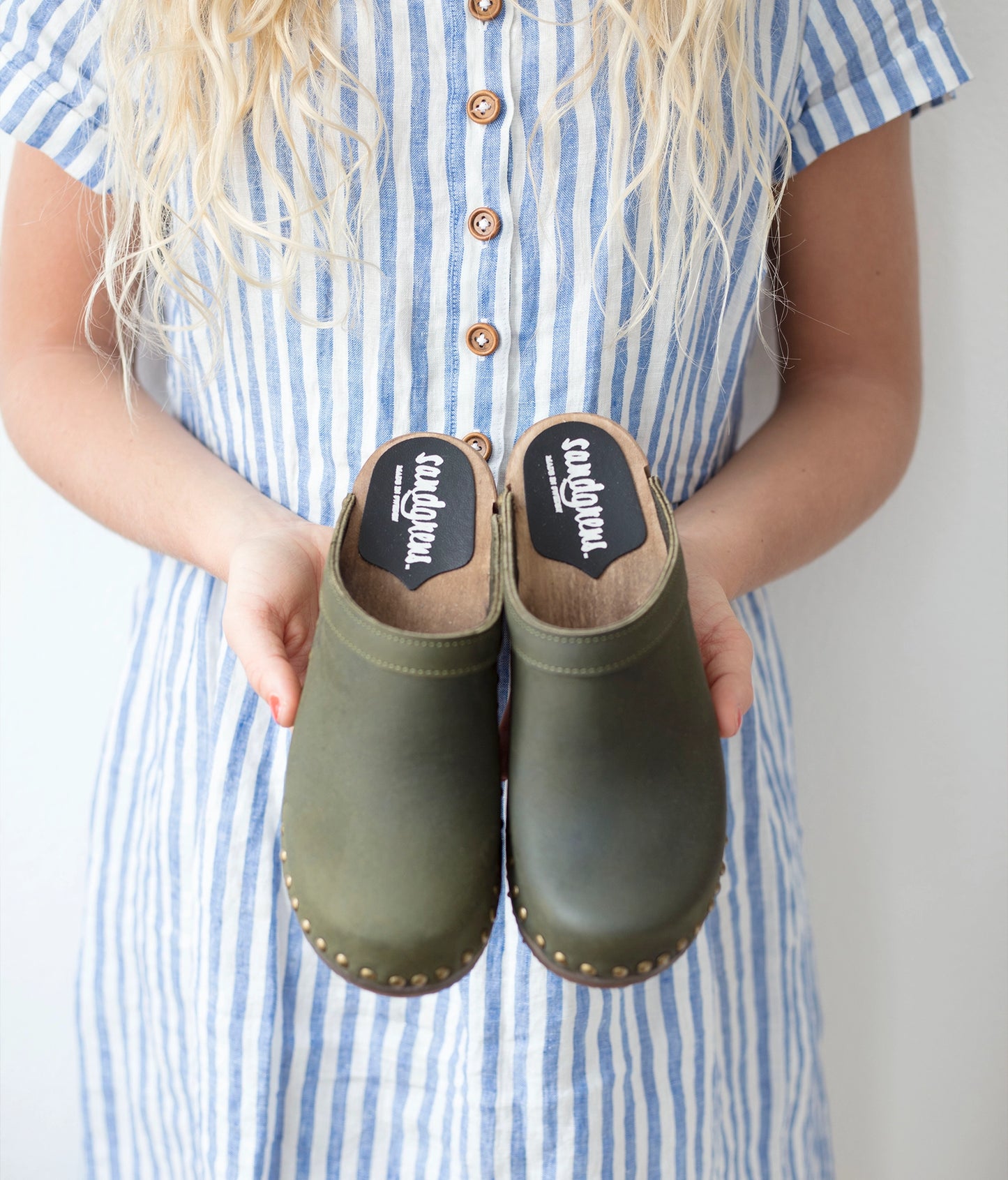 low heeled clog mules in olive nubuck leather stapled on a dark wooden base with brass gold studs