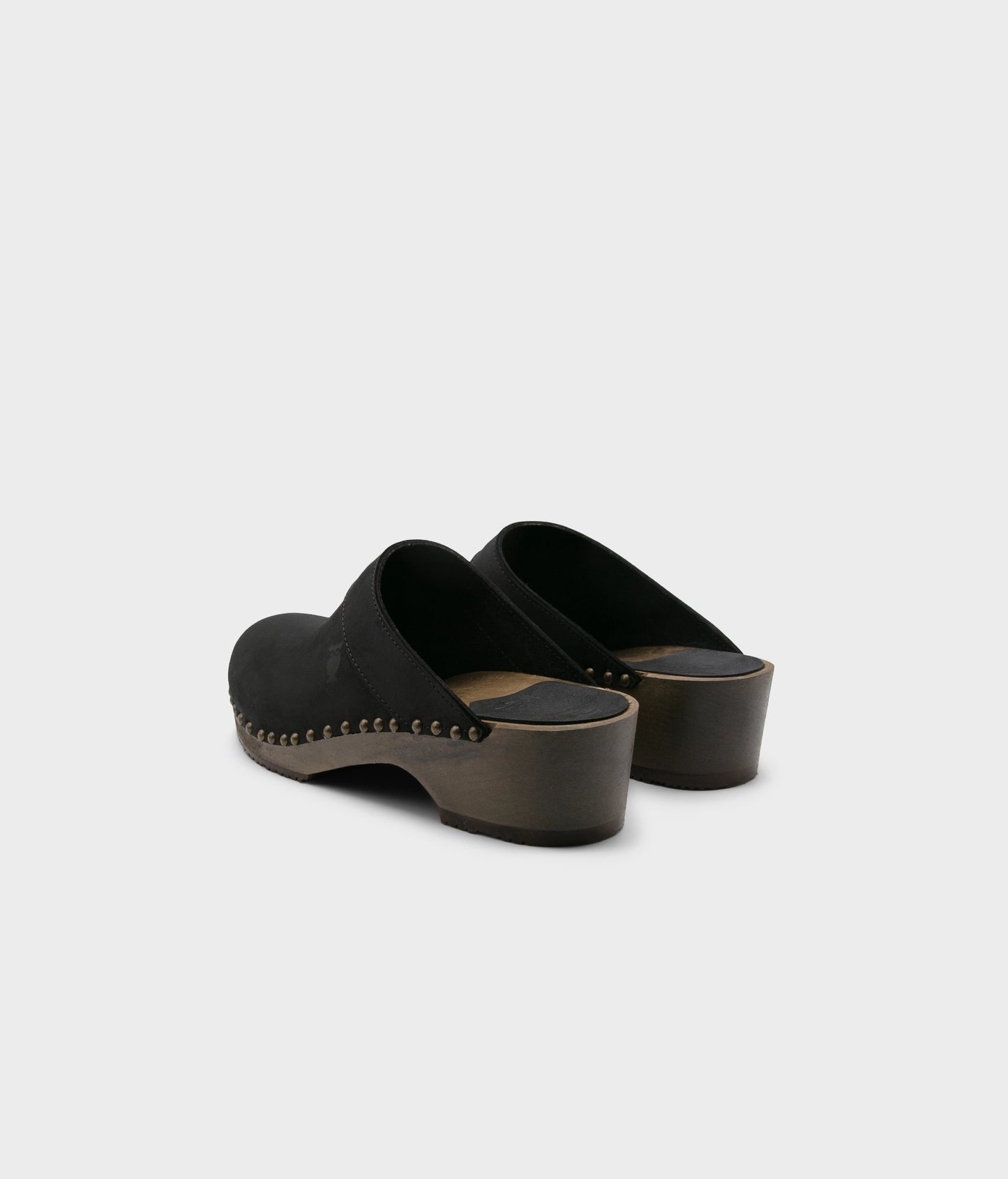 low heeled clog mules in black nubuck leather stapled on a dark wooden base with brass gold studs