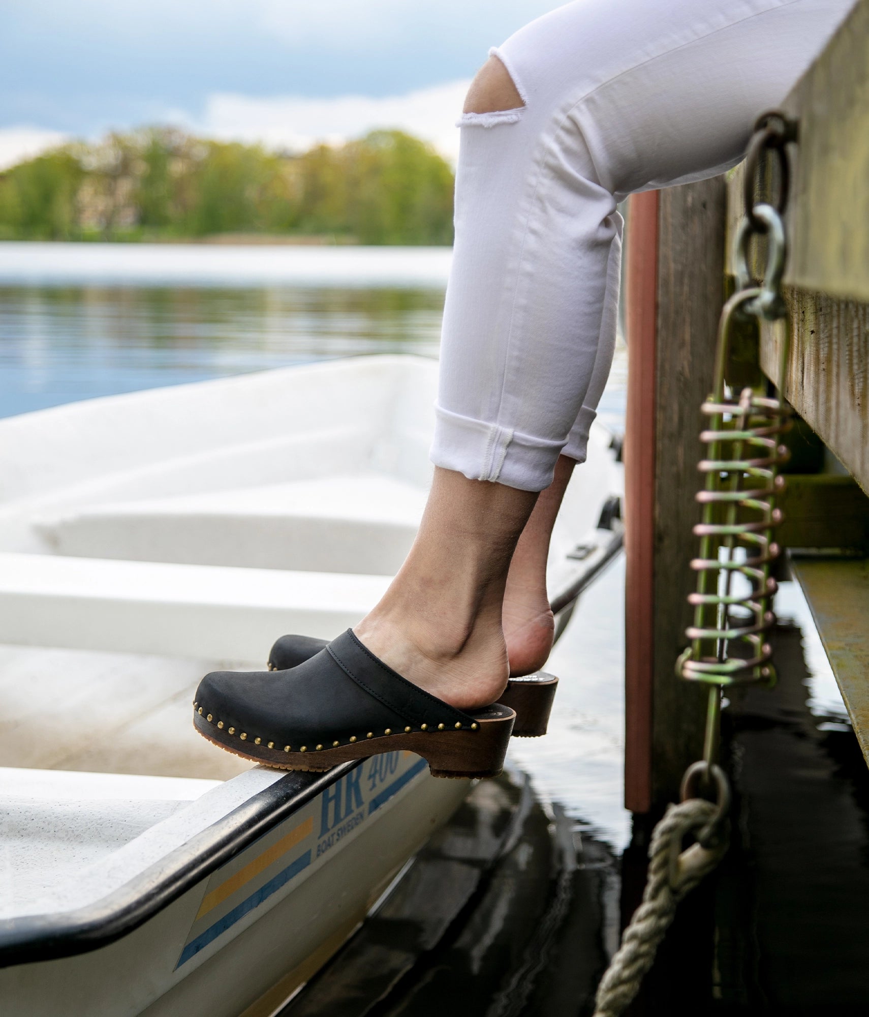 low heeled clog mules in black nubuck leather stapled on a dark wooden base with brass gold studs