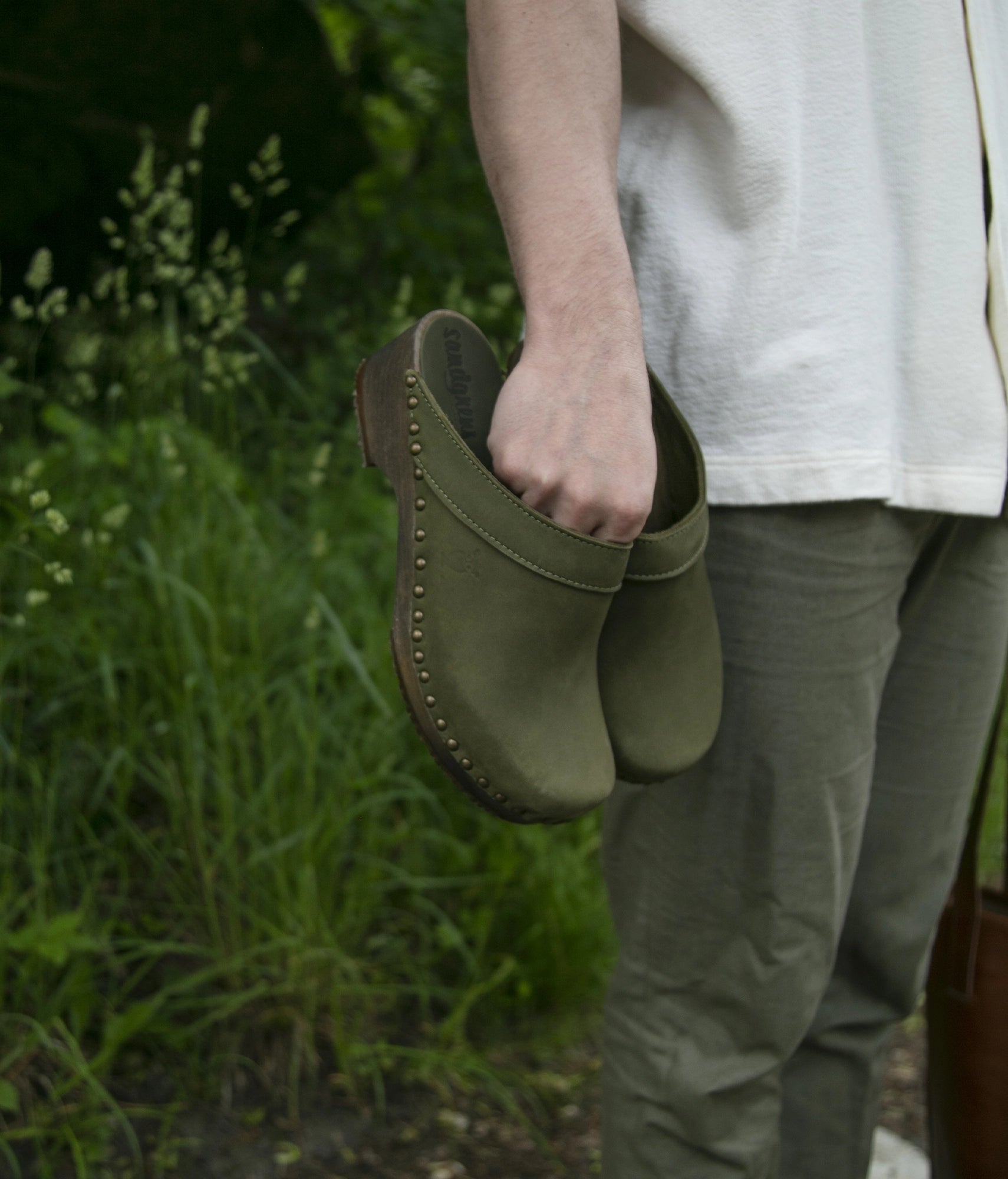 low heeled clog mules in olive green nubuck leather stapled on a dark wooden base with brass gold studs