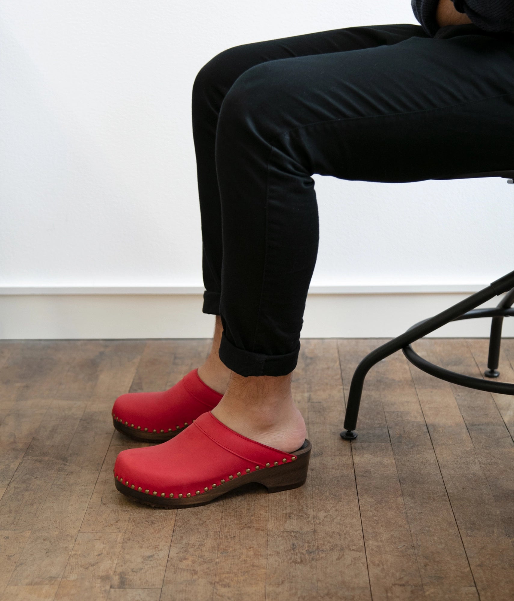 low heeled clog mules in red nubuck leather stapled on a dark wooden base with brass gold studs