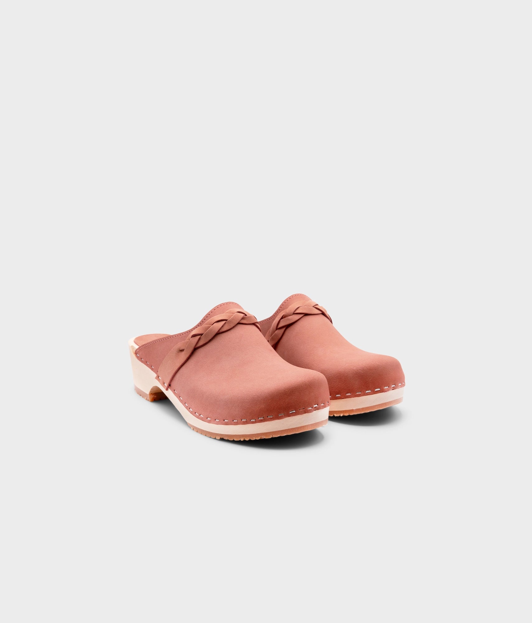 low heeled clog mules in blush pink nubuck leather with a braided strap stapled on a light wooden base