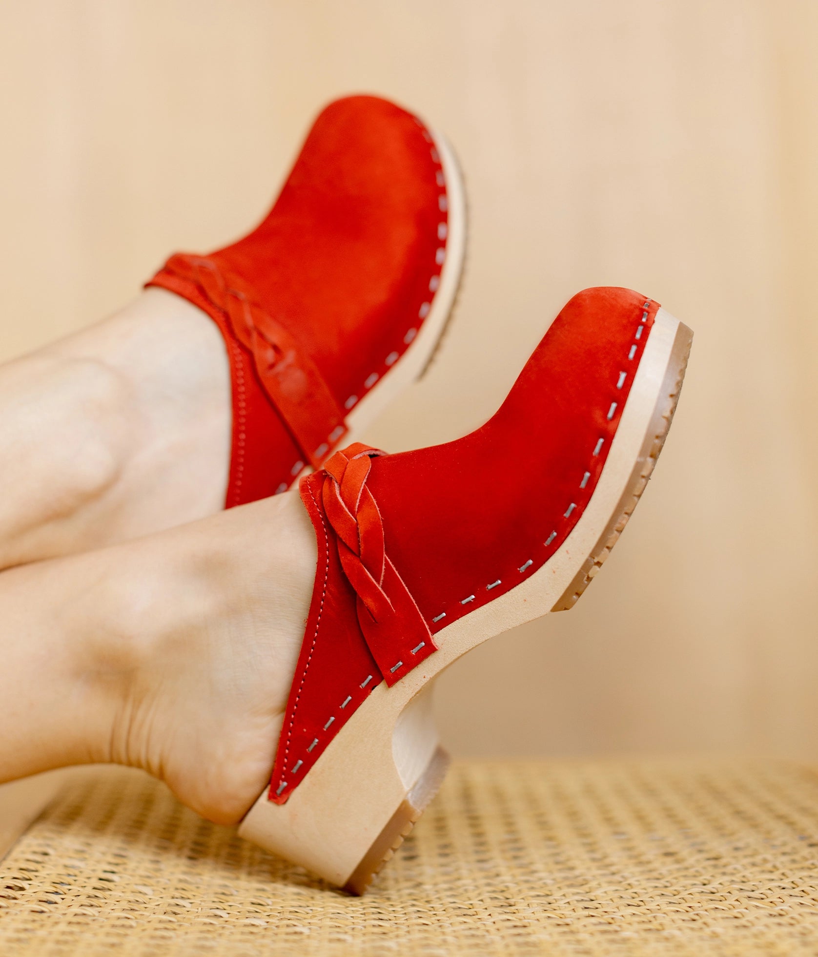 low heeled clog mules in red nubuck leather with a braided strap stapled on a light wooden base