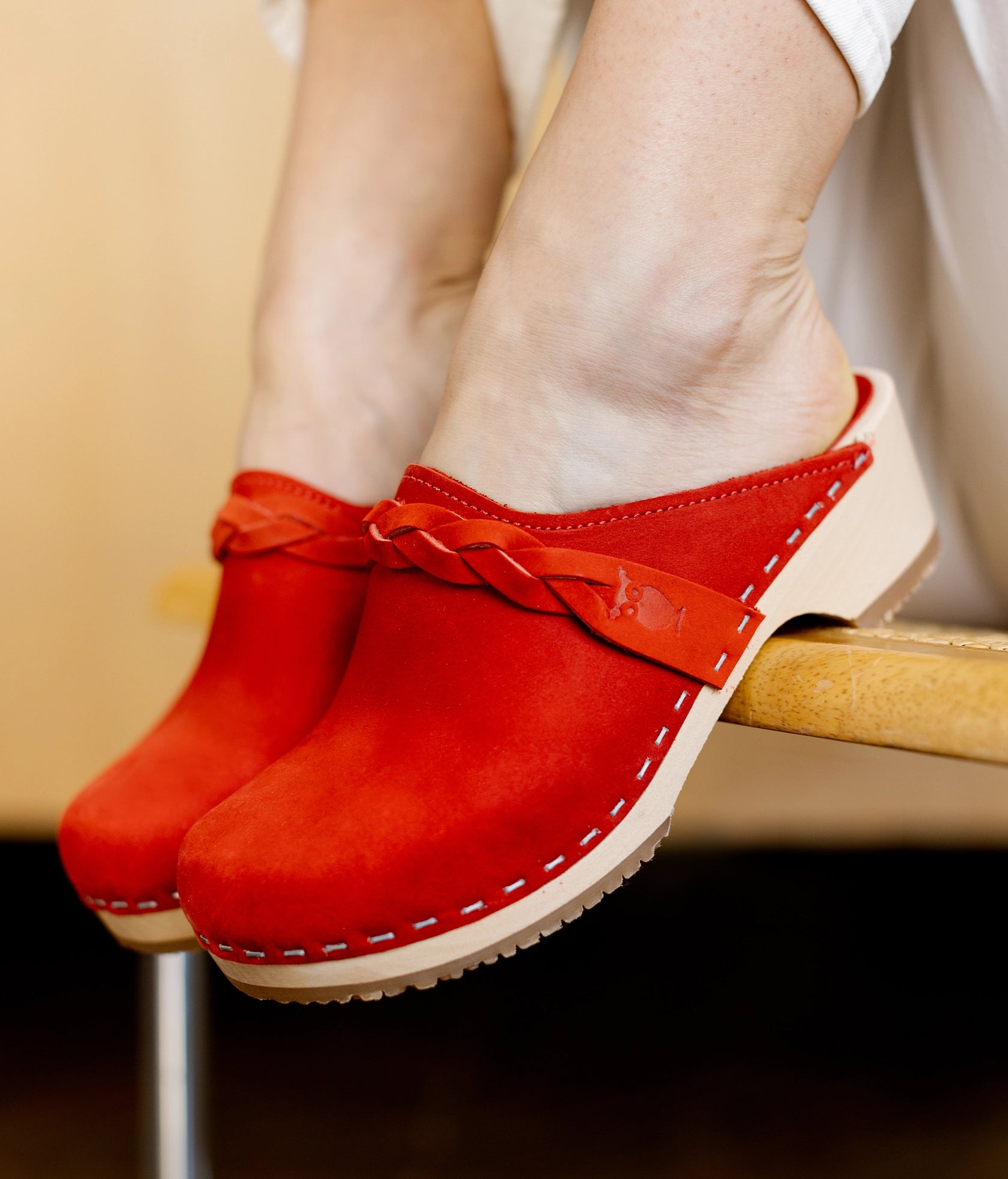low heeled clog mules in red nubuck leather with a braided strap stapled on a light wooden base