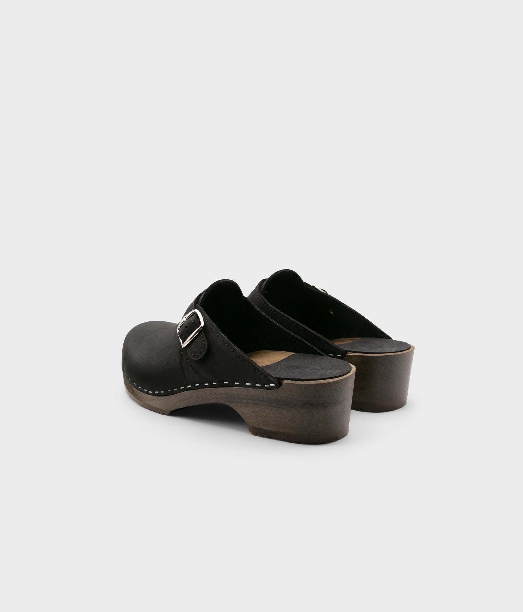 men's clog mule in black nubuck leather stapled on a dark wooden base with a silver buckle on top