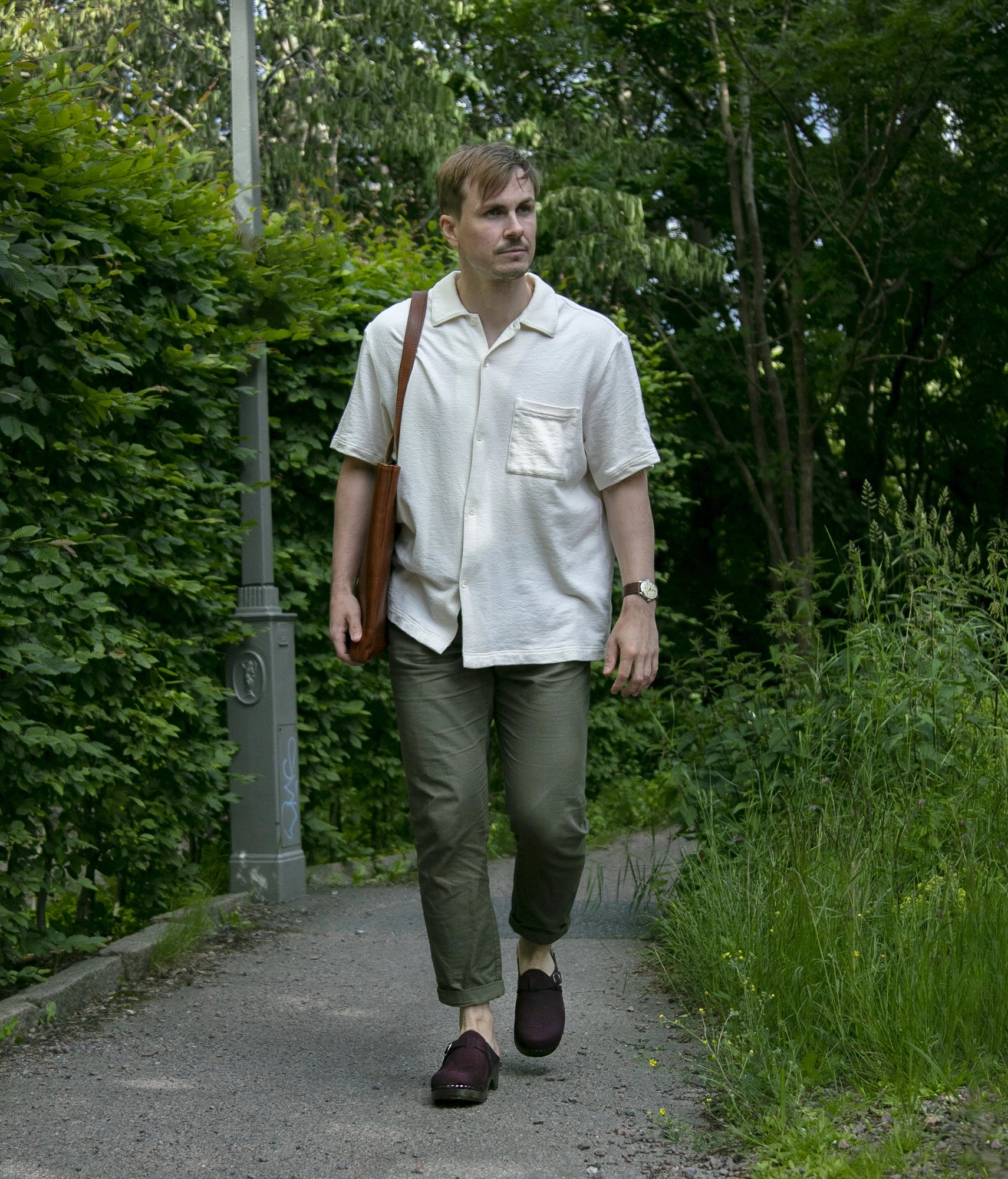 Man walking in clog mule with purple plum nubuck leather stapled on a dark wooden base with a silver buckle on top