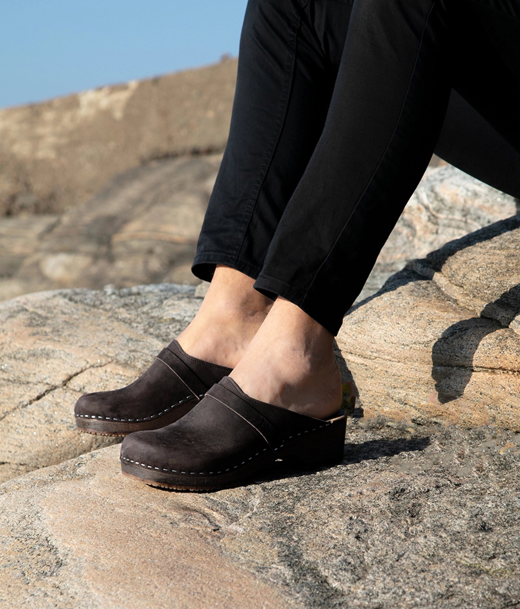 low heeled classic clog mules in black nubuck leather stapled on a dark wooden base