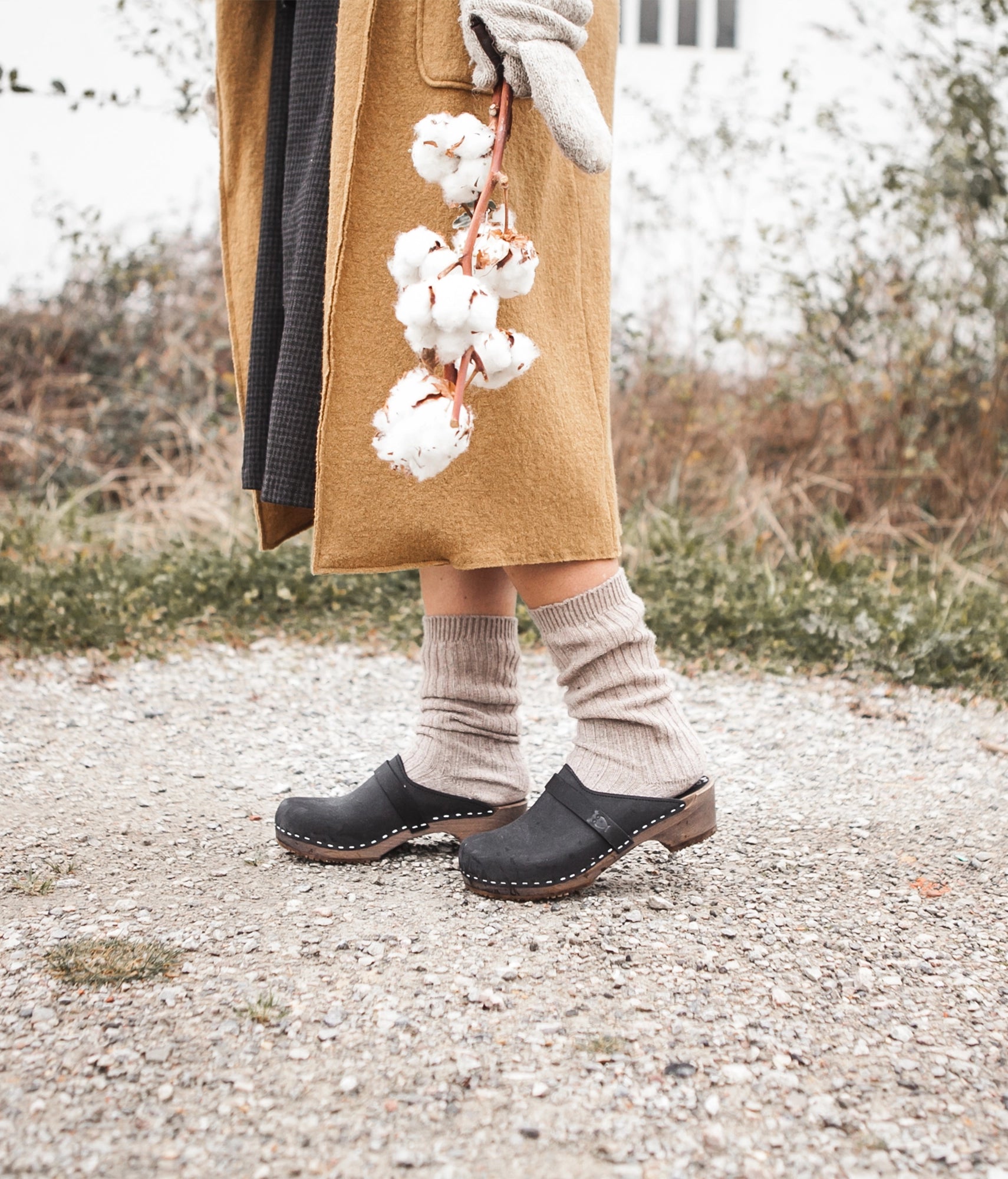 classic low heeled clog mule in black nubuck leather stapled on a dark wooden base with a leather strap
