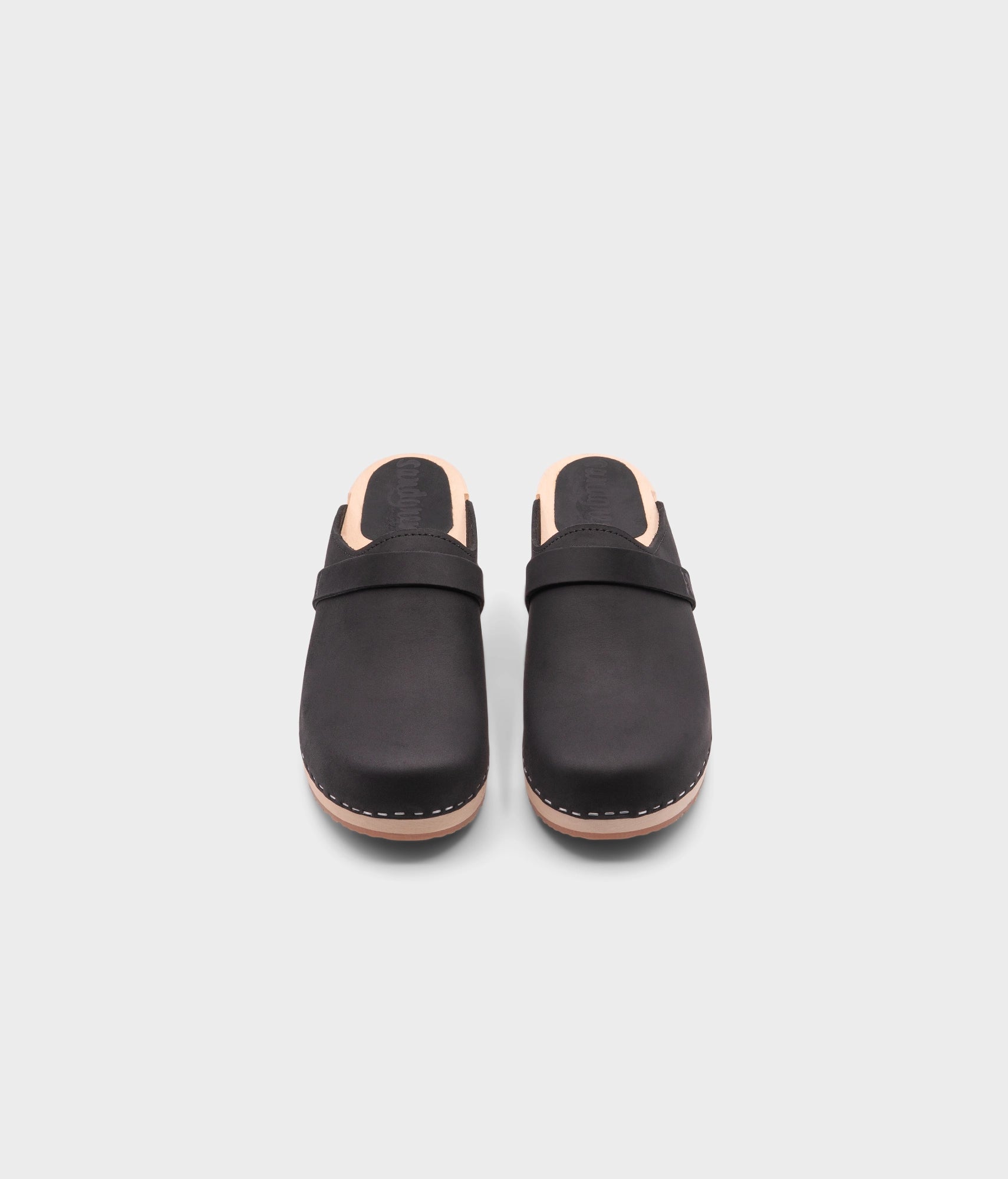 classic low heeled clog mule in black nubuck leather stapled on a light wooden base with a leather strap