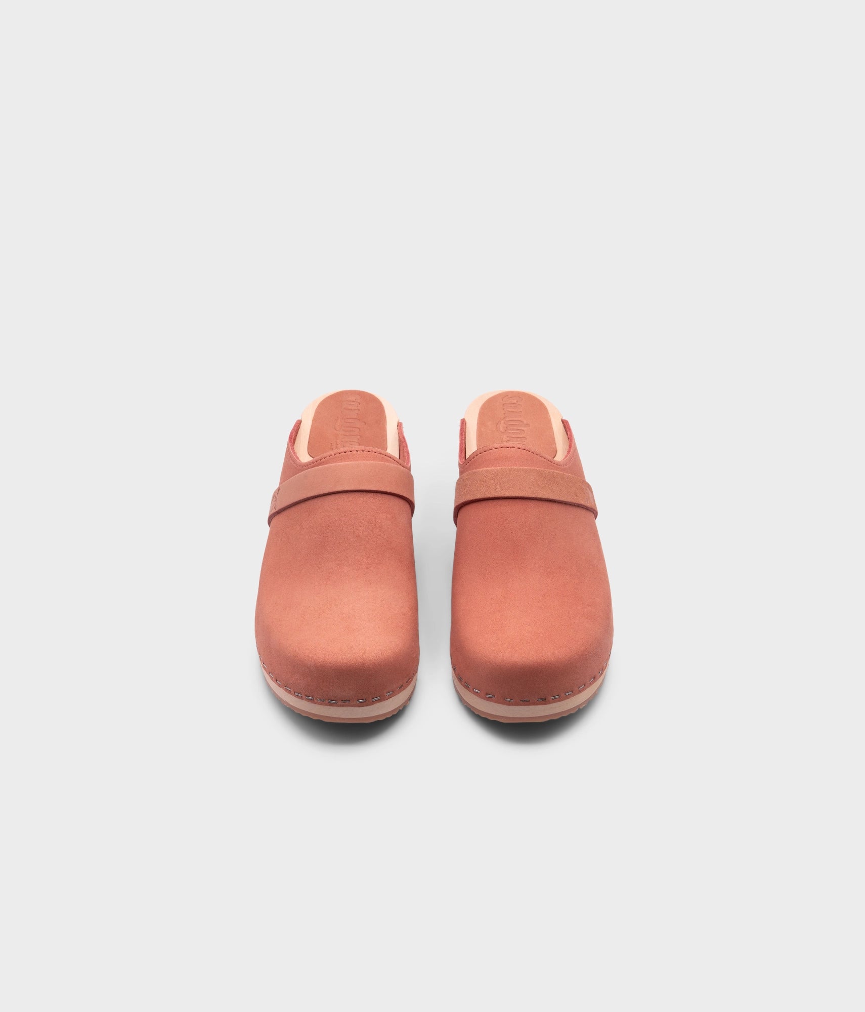 classic low heeled clog mule in blush pink nubuck leather stapled on a light wooden base with a leather strap