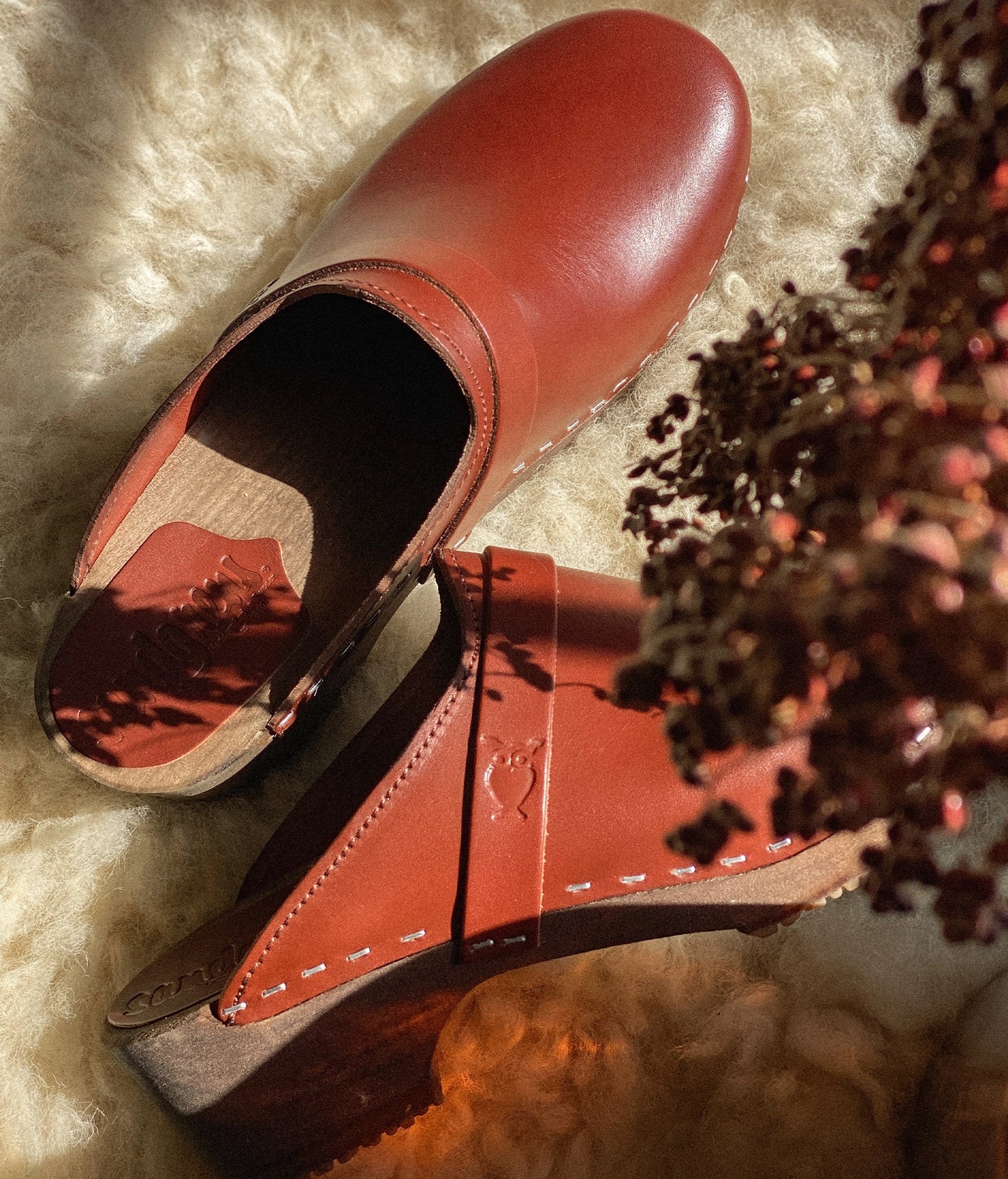 classic low heeled clog mule in cognac red vegetable tanned leather stapled on a dark wooden base with a leather strap