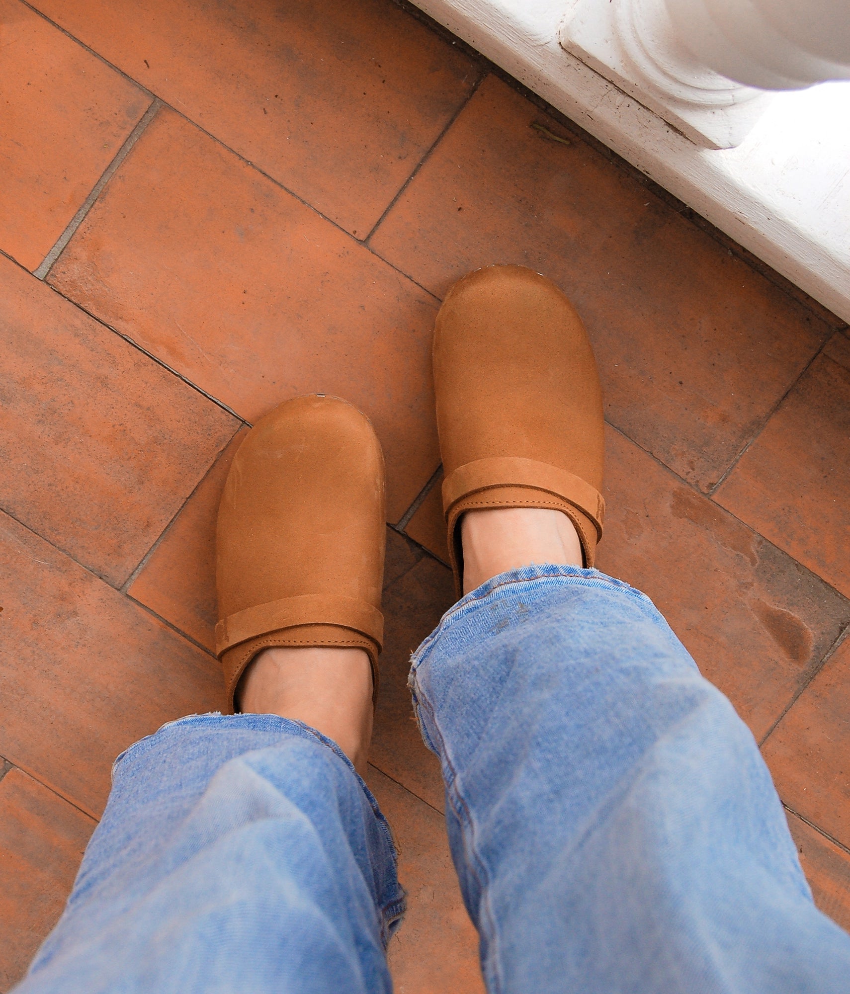 classic low heeled clog mule in light brown nubuck leather stapled on a dark wooden base with a leather strap