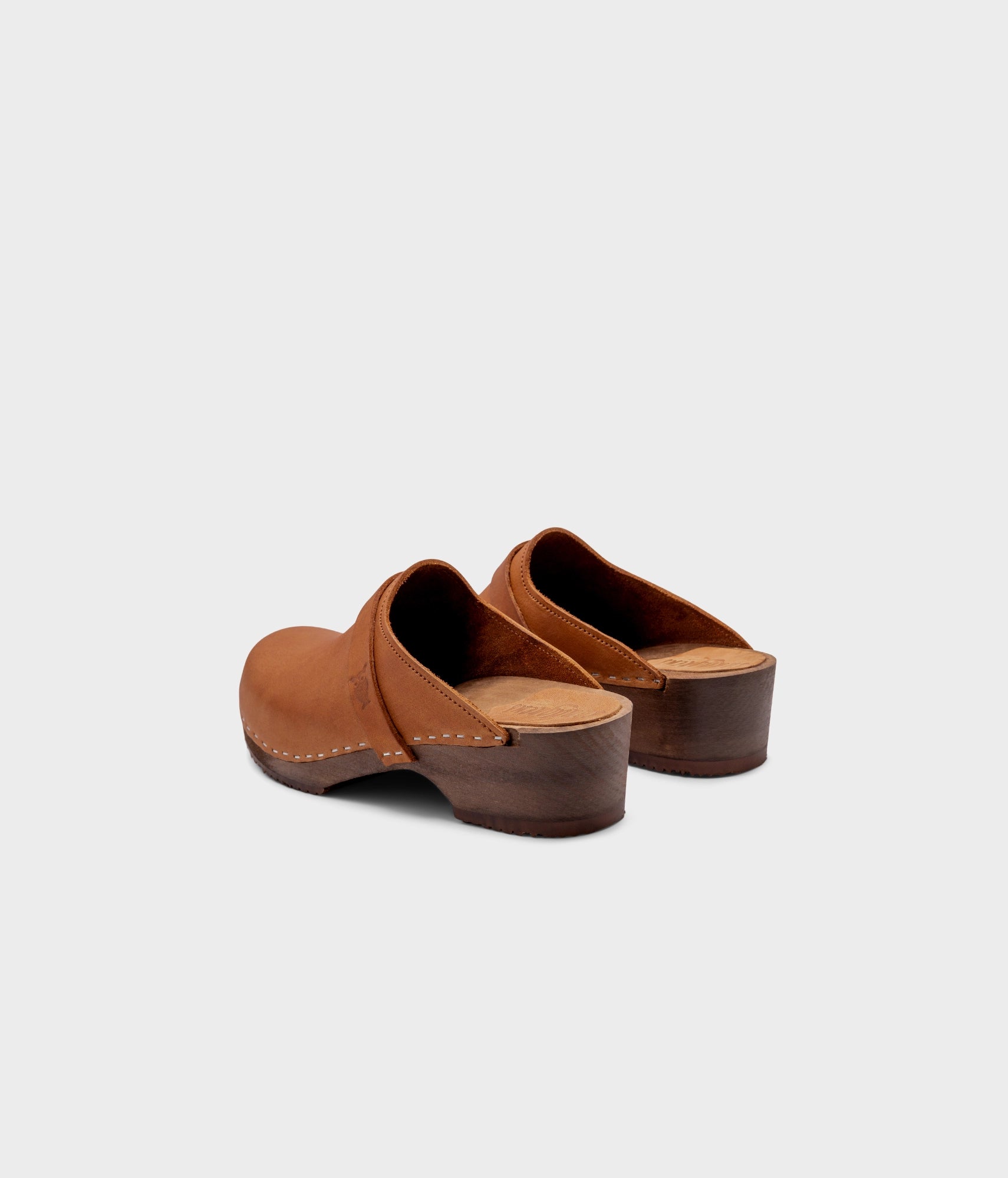 classic low heeled clog mule in light brown nubuck leather stapled on a dark wooden base with a leather strap