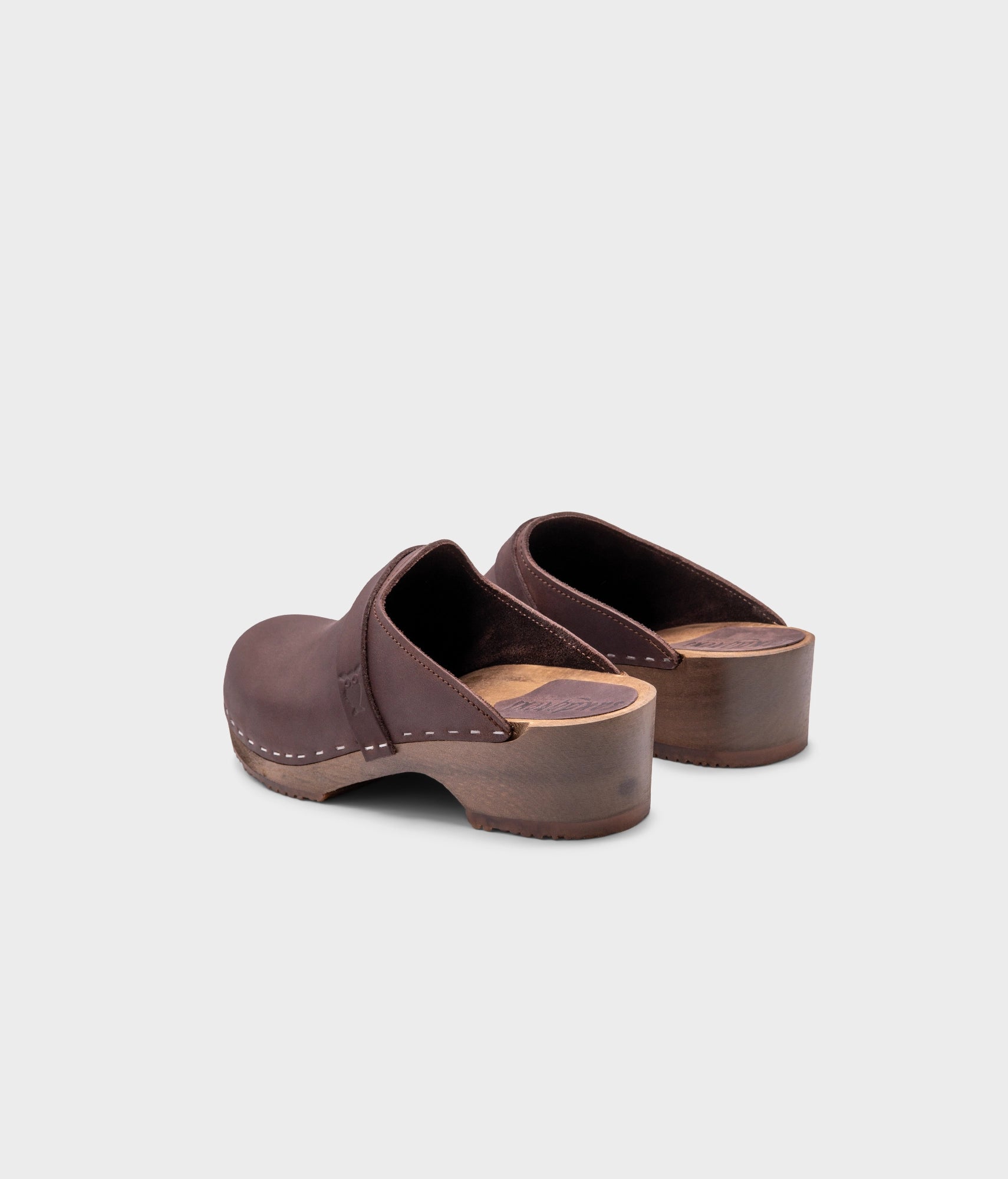 classic low heeled clog mule in dark brown nubuck leather stapled on a dark wooden base with a leather strap