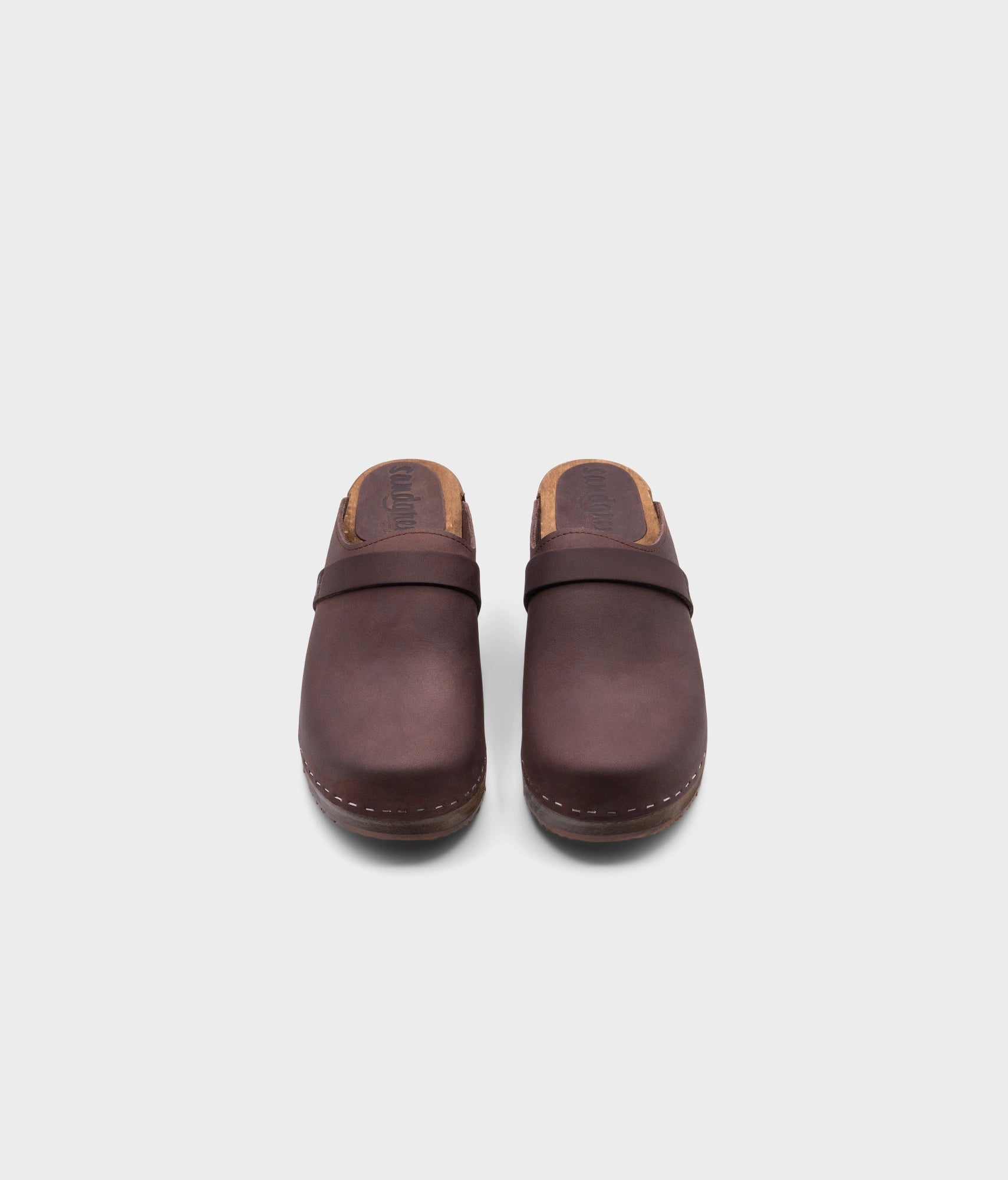 classic low heeled clog mule in dark brown nubuck leather stapled on a dark wooden base with a leather strap