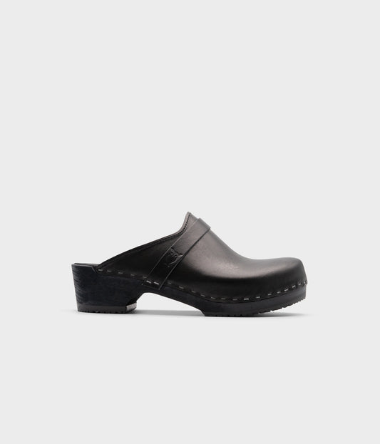 classic low heeled clog mule in black vegetable tanned leather stapled on a black wooden base with a leather strap