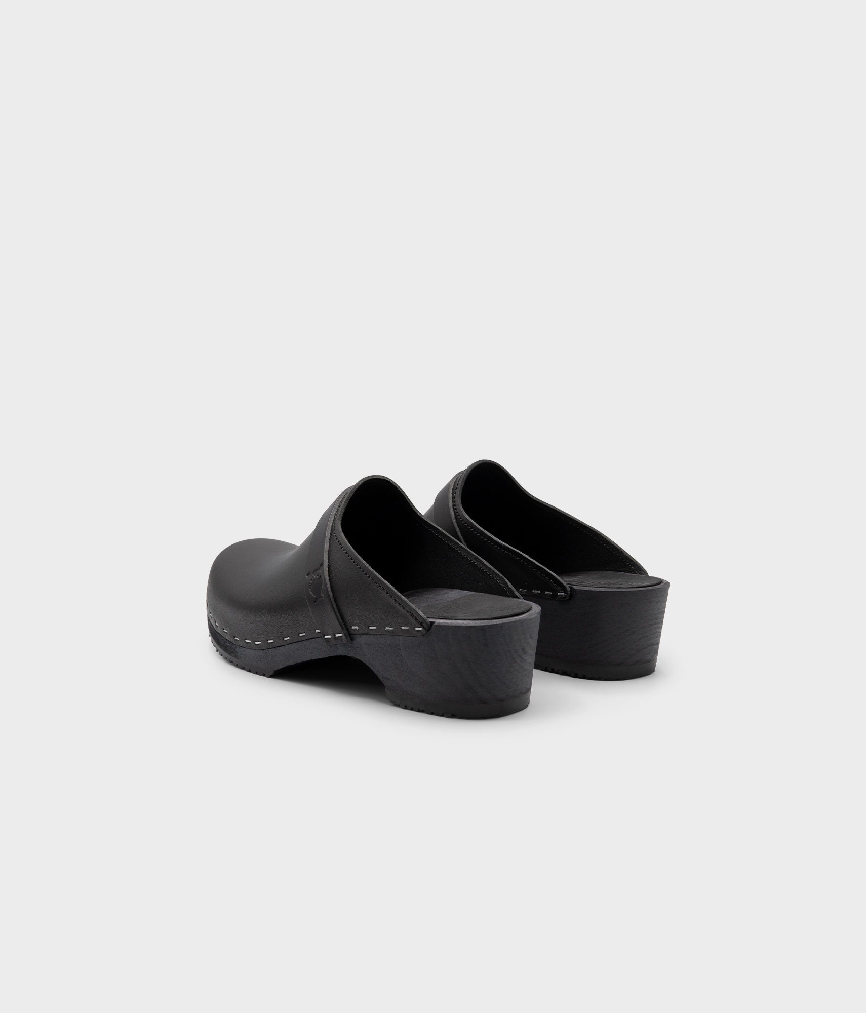 classic low heeled clog mule in black vegetable tanned leather stapled on a black wooden base with a leather strap