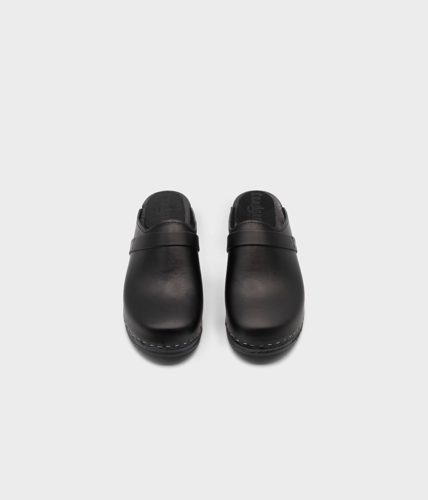 classic low heeled clog mule in black vegetable tanned leather stapled on a black wooden base with a leather strap