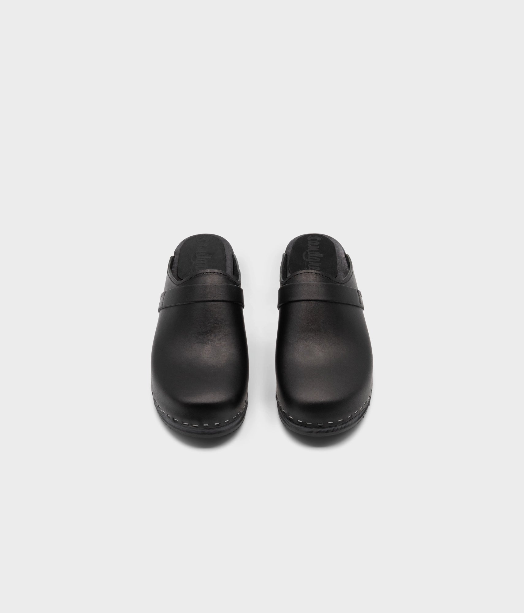 classic low heeled clog mule in black vegetable tanned leather stapled on a black wooden base with a leather strap