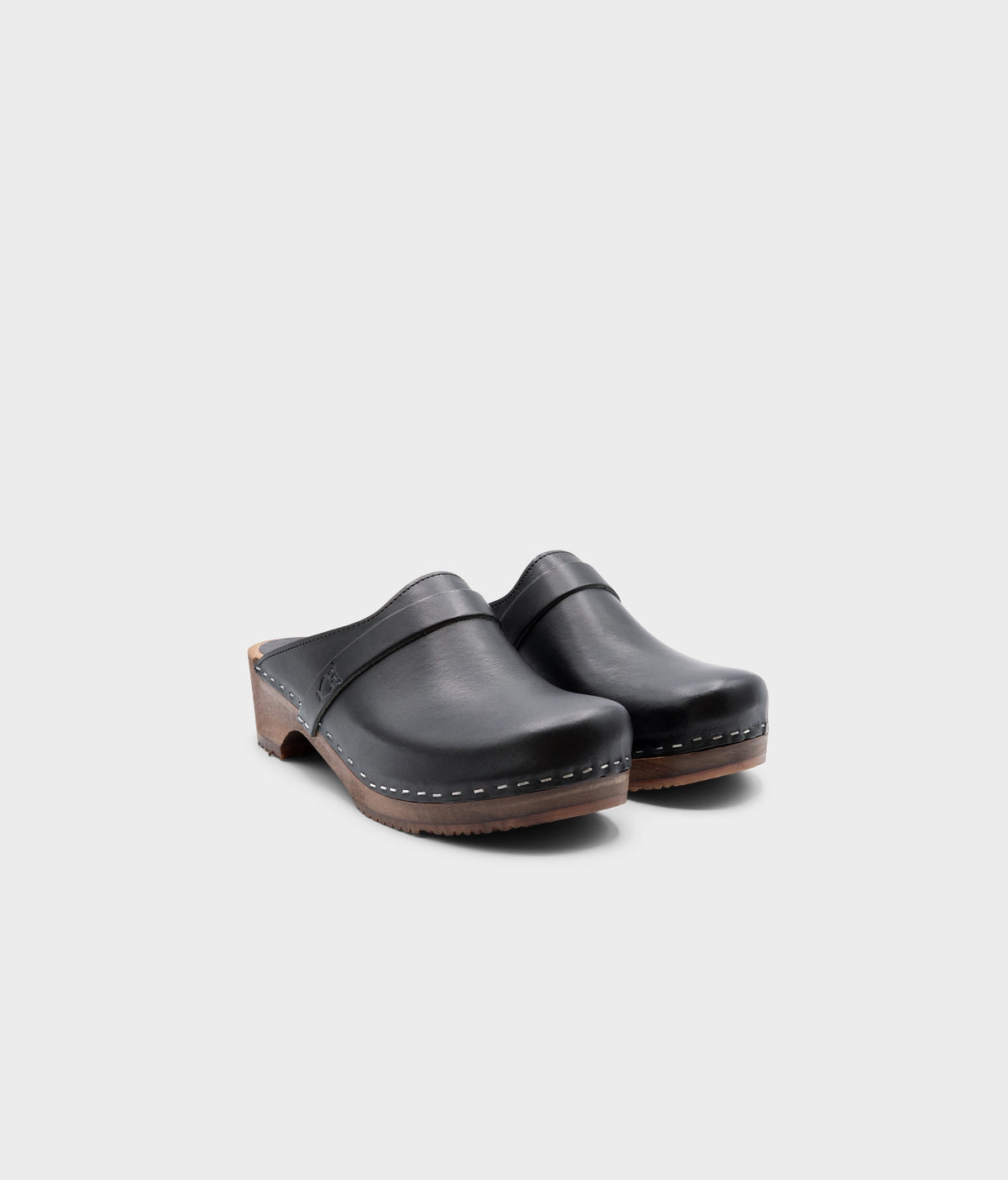 classic low heeled clog mule in black vegetable tanned leather stapled on a dark wooden base with a leather strap