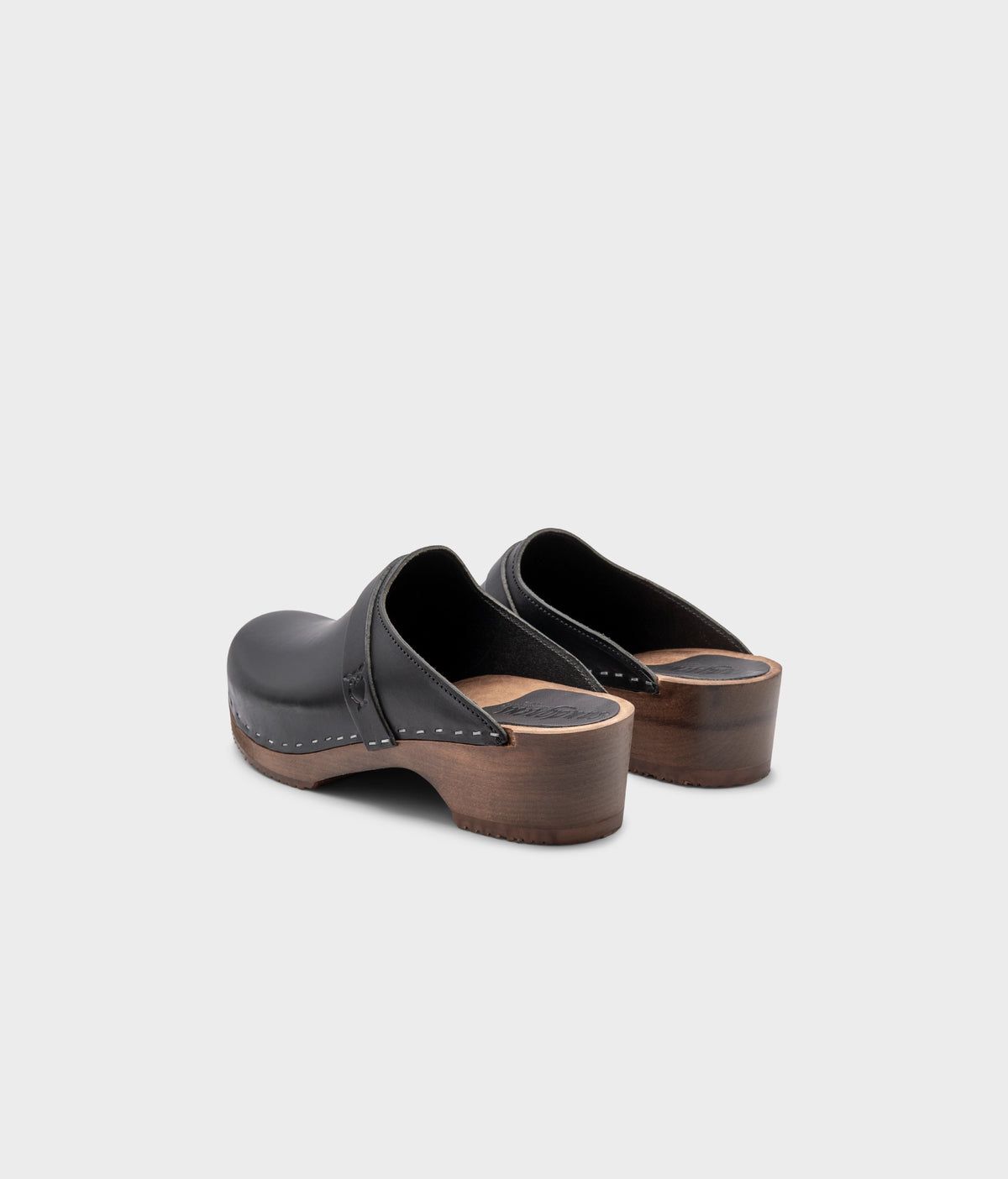classic low heeled clog mule in black vegetable tanned leather stapled on a dark wooden base with a leather strap