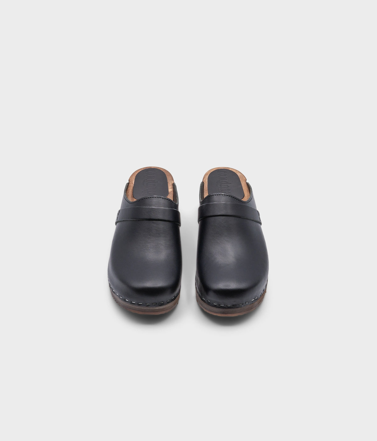 classic low heeled clog mule in black vegetable tanned leather stapled on a dark wooden base with a leather strap
