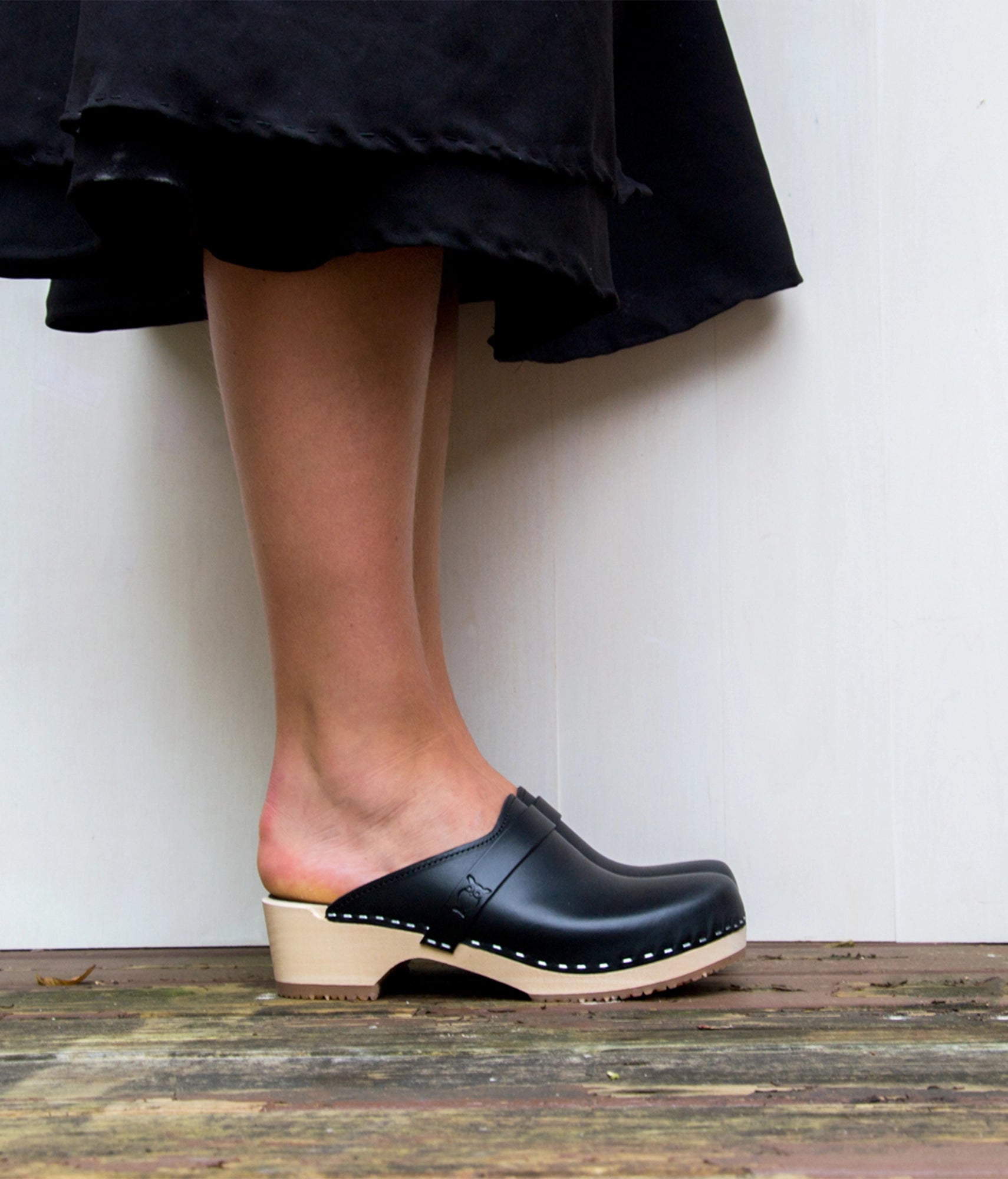 classic low heeled clog mule in black vegetable tanned leather stapled on a light wooden base with a leather strap