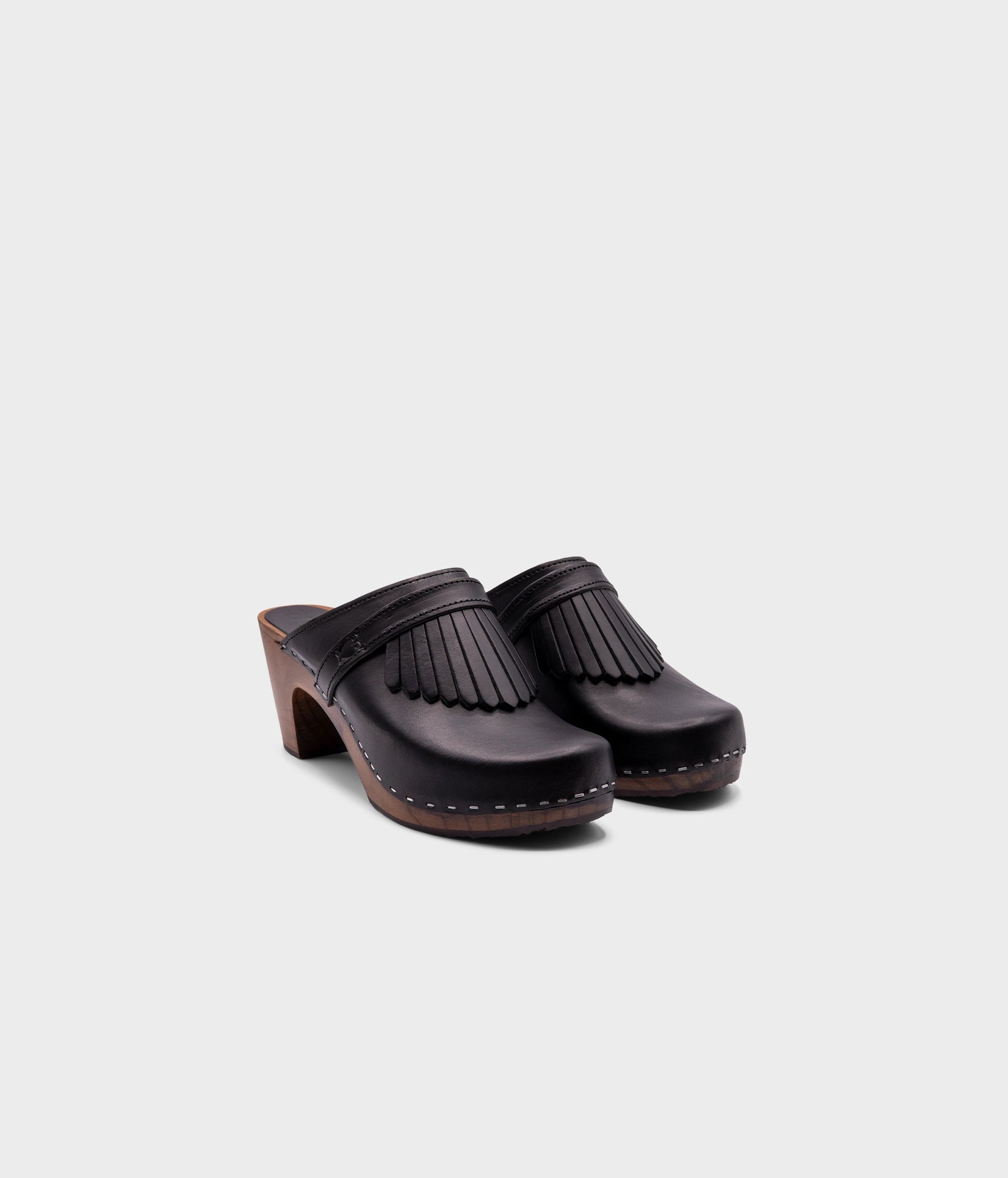 high rise clog mule in black vegetable tanned leather stapled on a dark wooden base with a leather strap with fringes