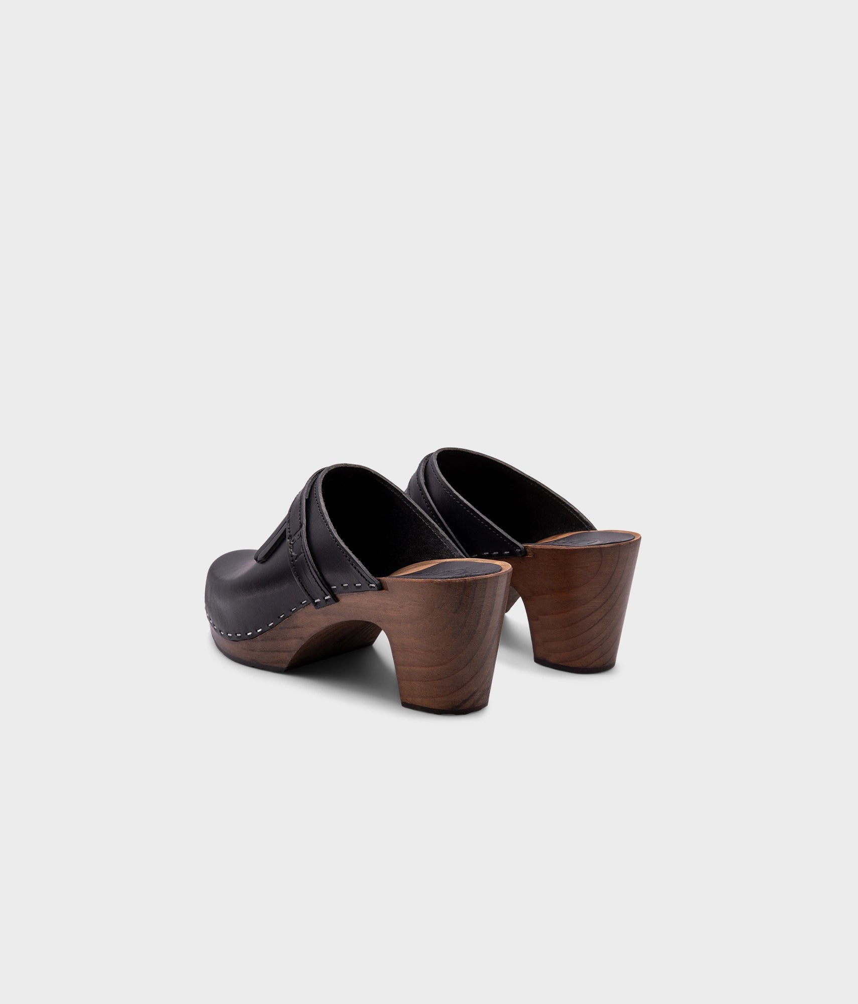 high rise clog mule in black vegetable tanned leather stapled on a dark wooden base with a leather strap with fringes