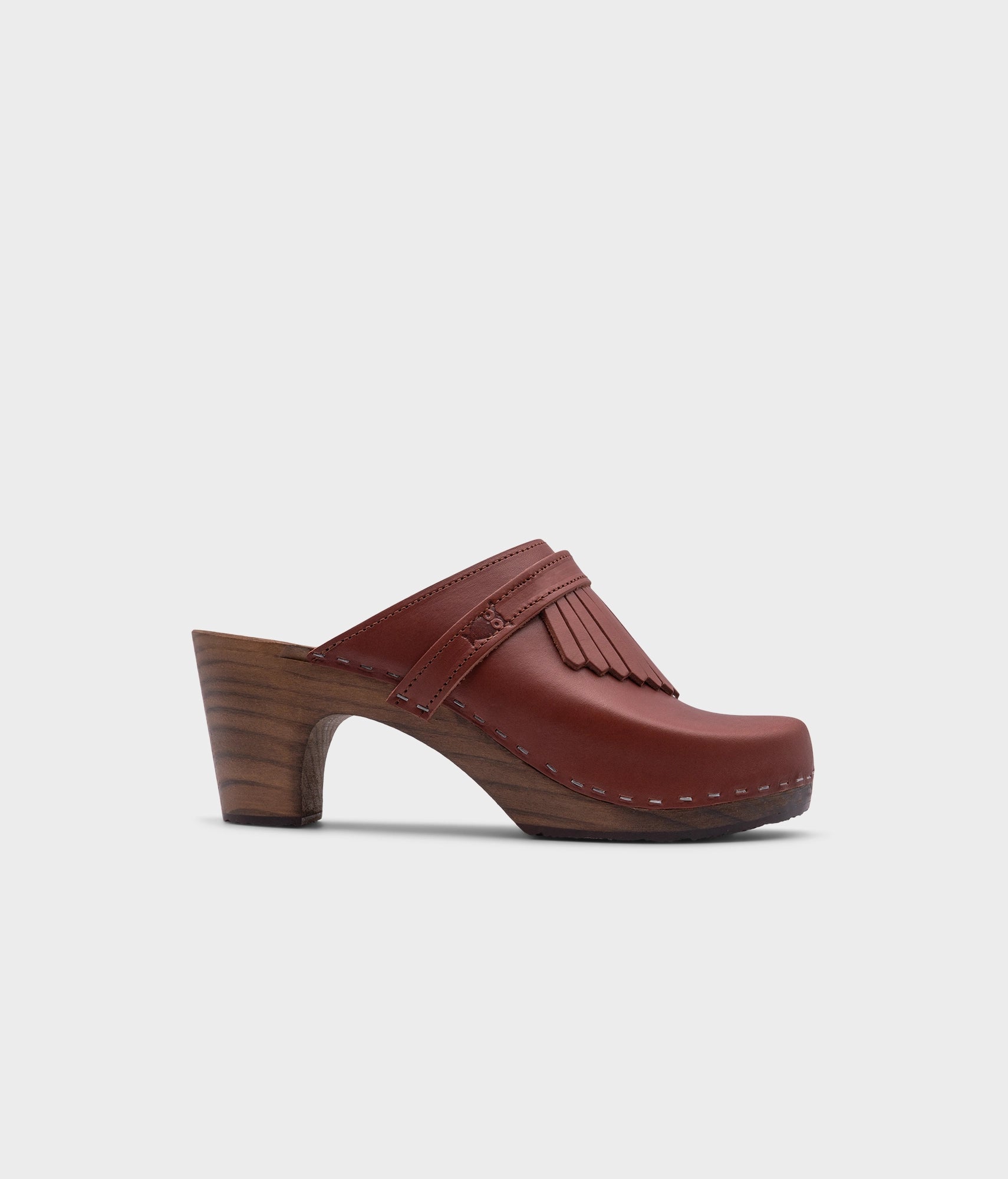 high rise clog mule in cognac red vegetable tanned leather stapled on a dark wooden base with a leather strap with fringes
