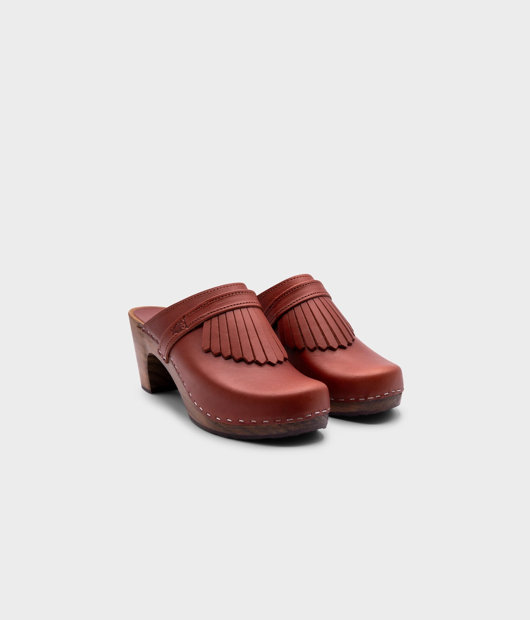 high rise clog mule in cognac red vegetable tanned leather stapled on a dark wooden base with a leather strap with fringes