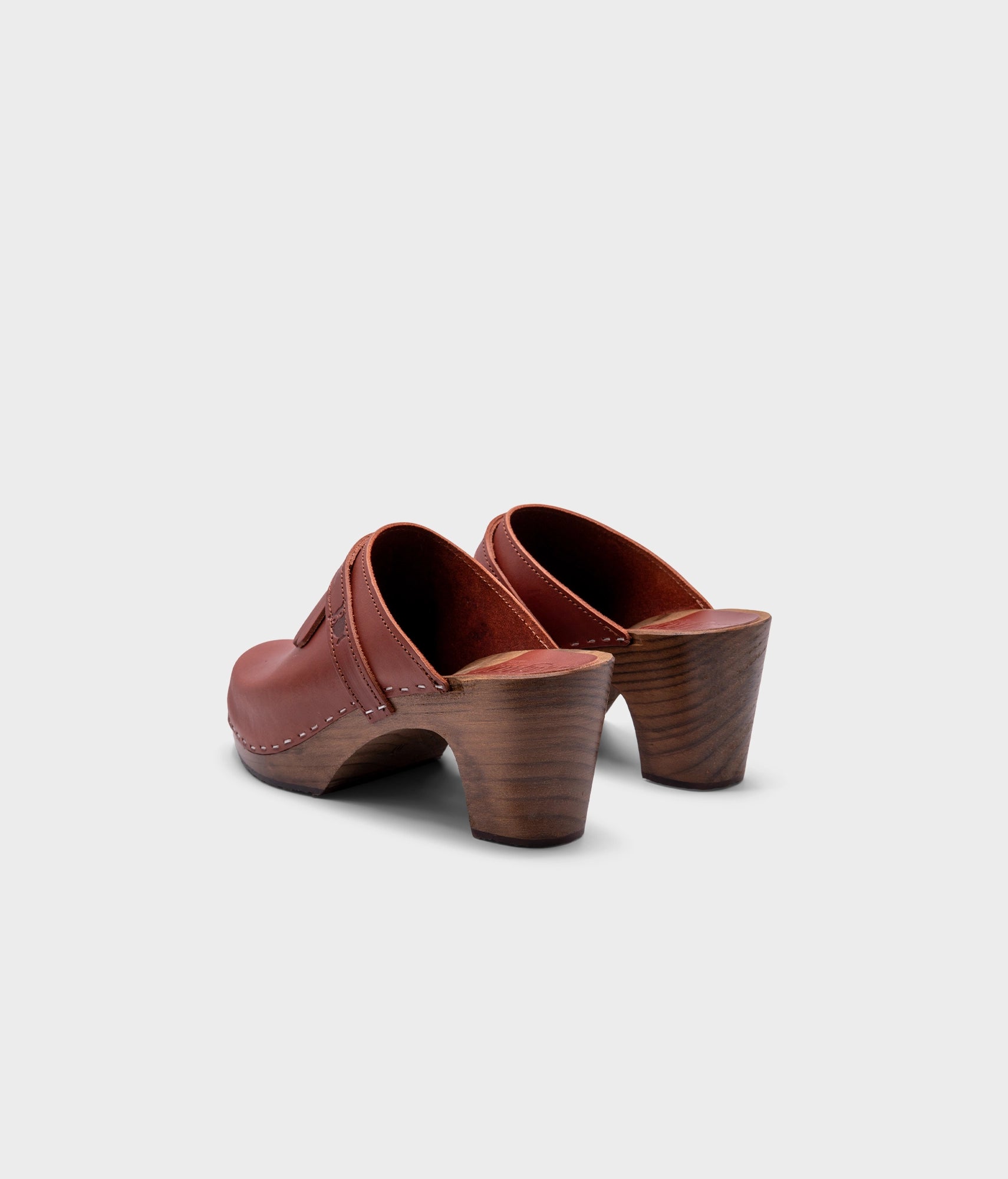 high rise clog mule in cognac red vegetable tanned leather stapled on a dark wooden base with a leather strap with fringes