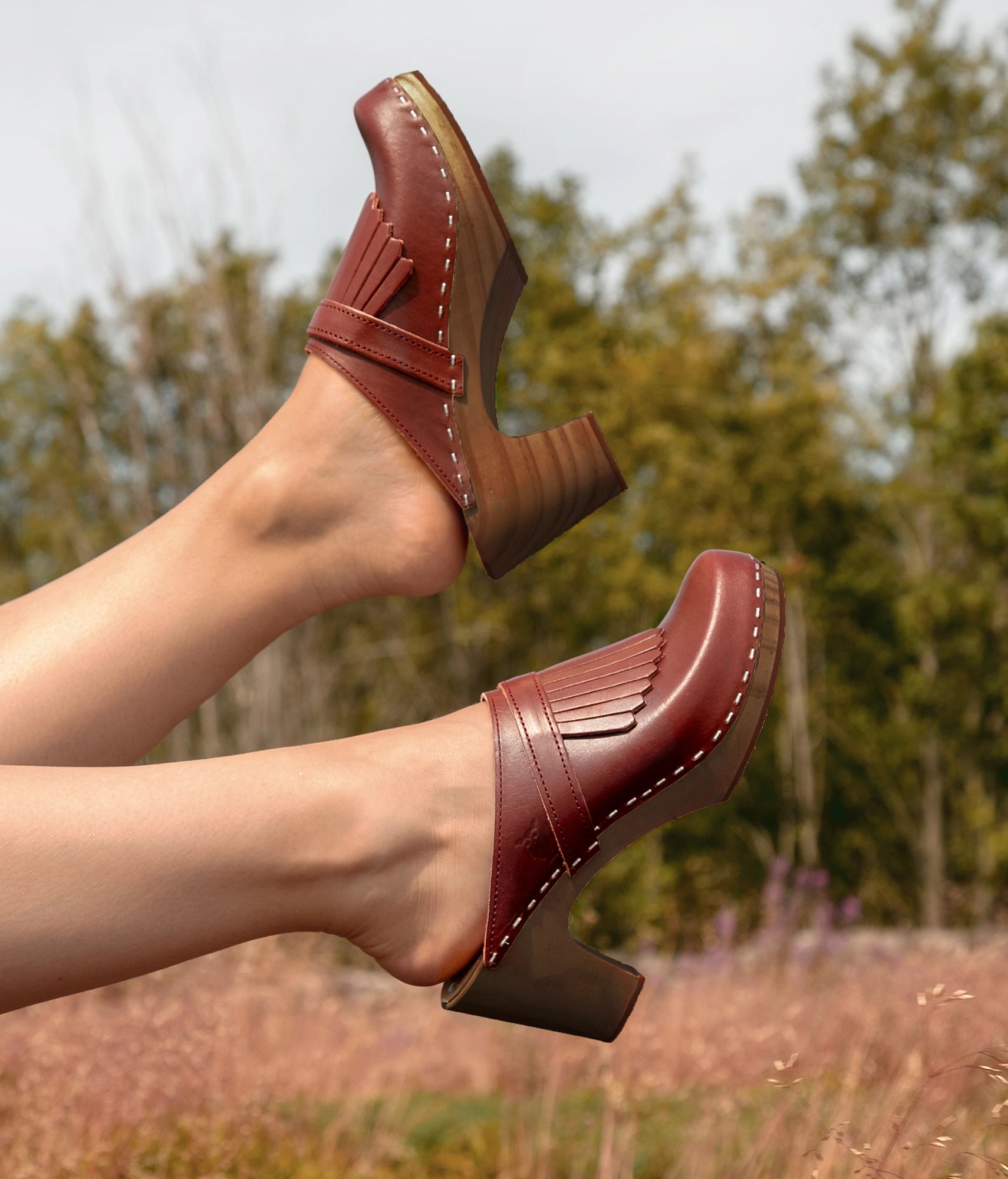 high rise clog mule in cognac red vegetable tanned leather stapled on a dark wooden base with a leather strap with fringes