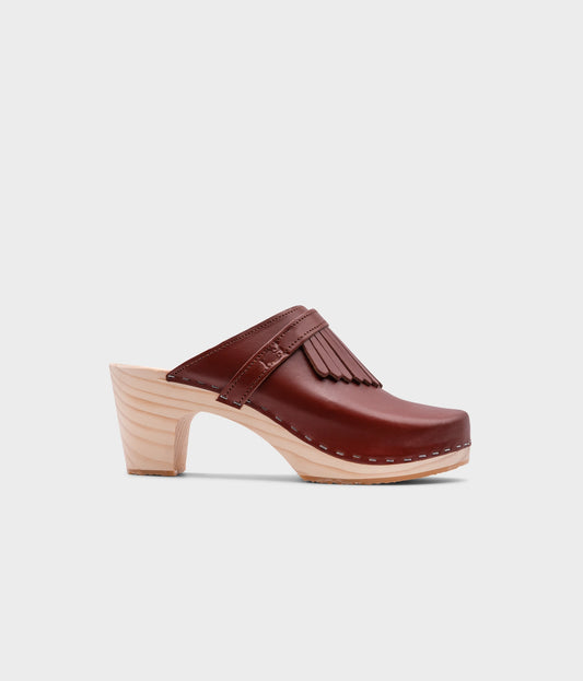 high rise clog mule in cognac red vegetable tanned leather stapled on a light wooden base with a leather strap with fringes