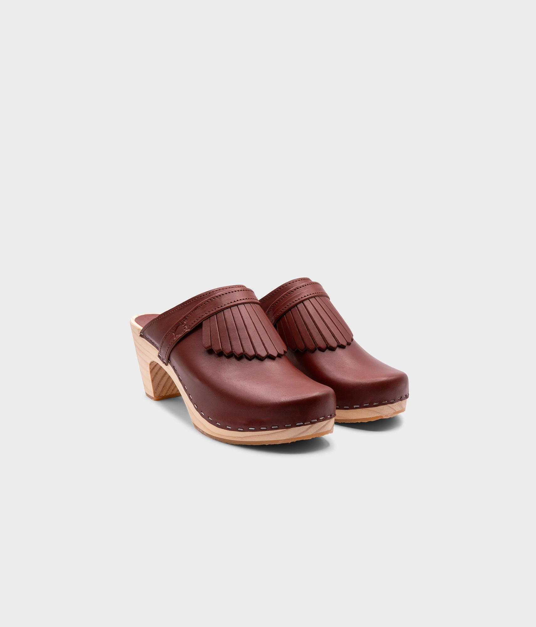 high rise clog mule in cognac red vegetable tanned leather stapled on a light wooden base with a leather strap with fringes