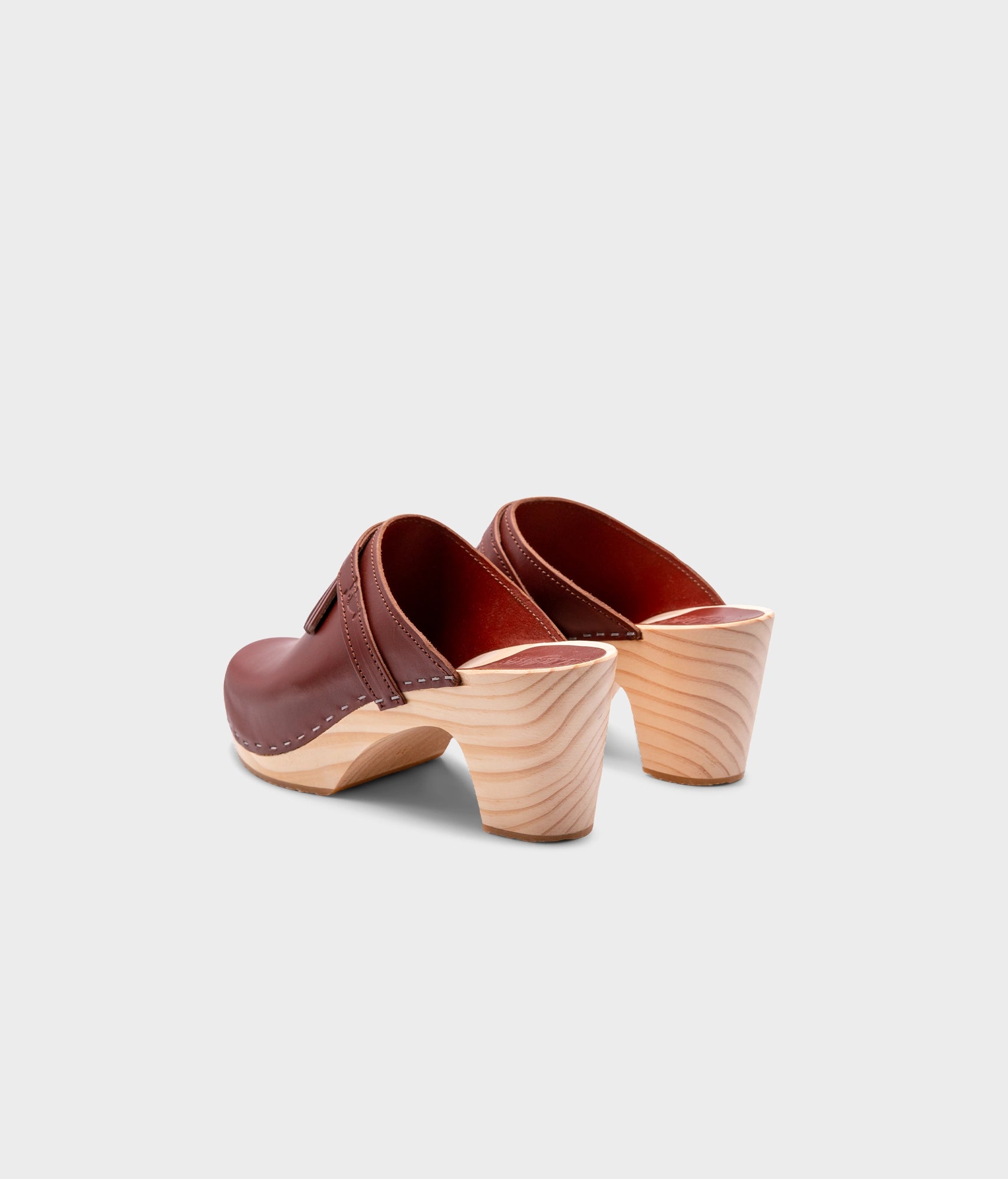 high rise clog mule in cognac red vegetable tanned leather stapled on a light wooden base with a leather strap with fringes