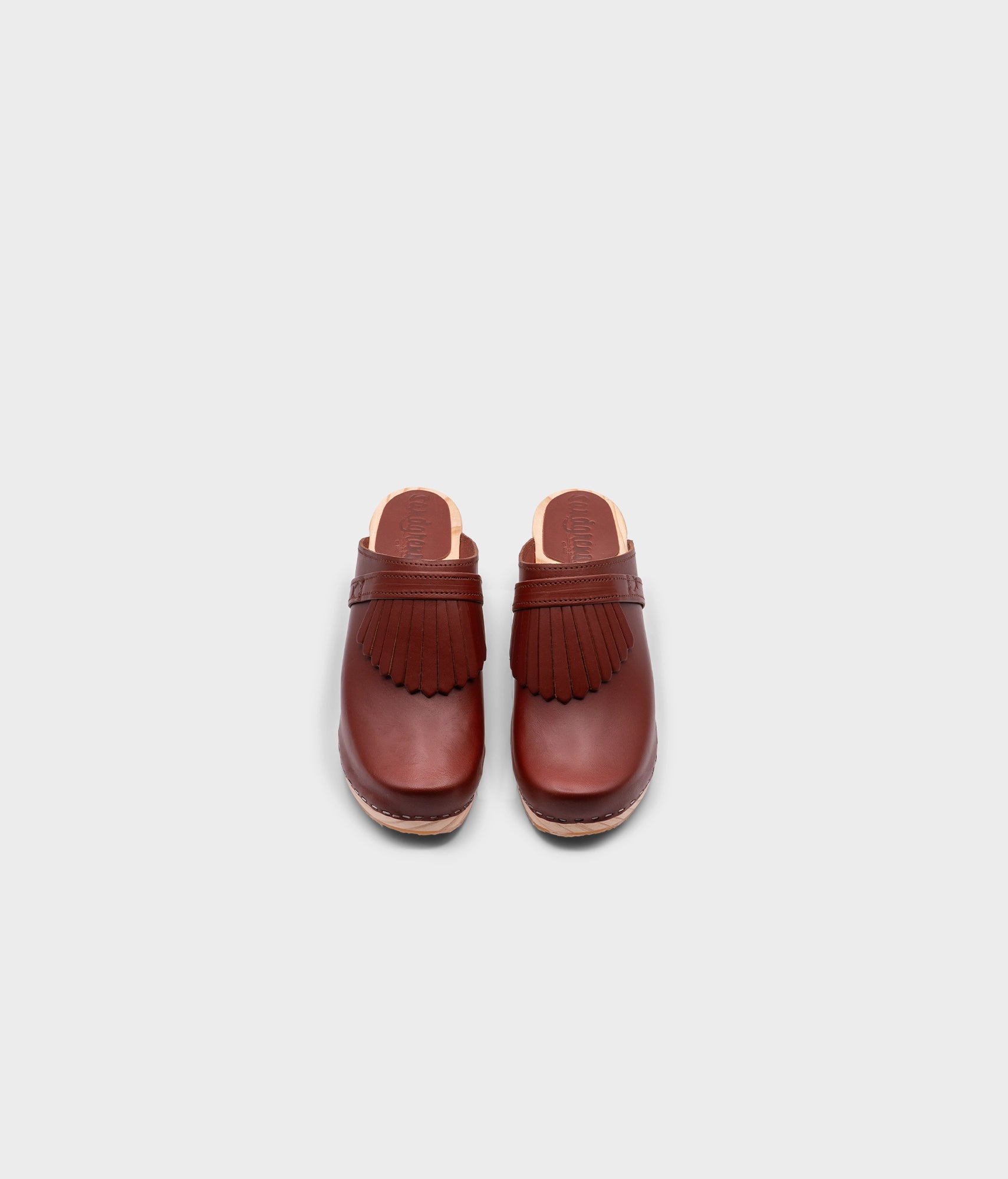 high rise clog mule in cognac red vegetable tanned leather stapled on a light wooden base with a leather strap with fringes
