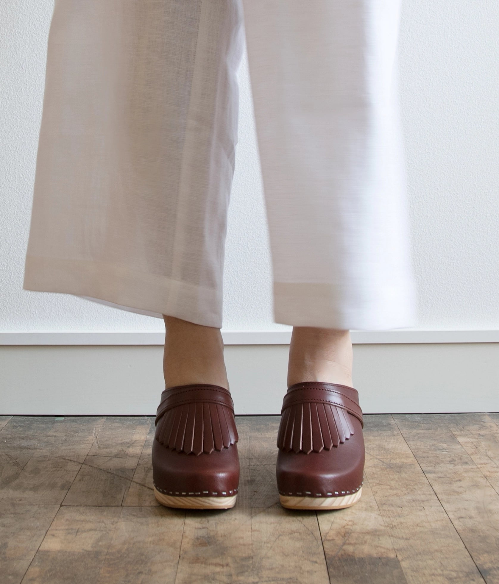 high rise clog mule in cognac red vegetable tanned leather stapled on a light wooden base with a leather strap with fringes