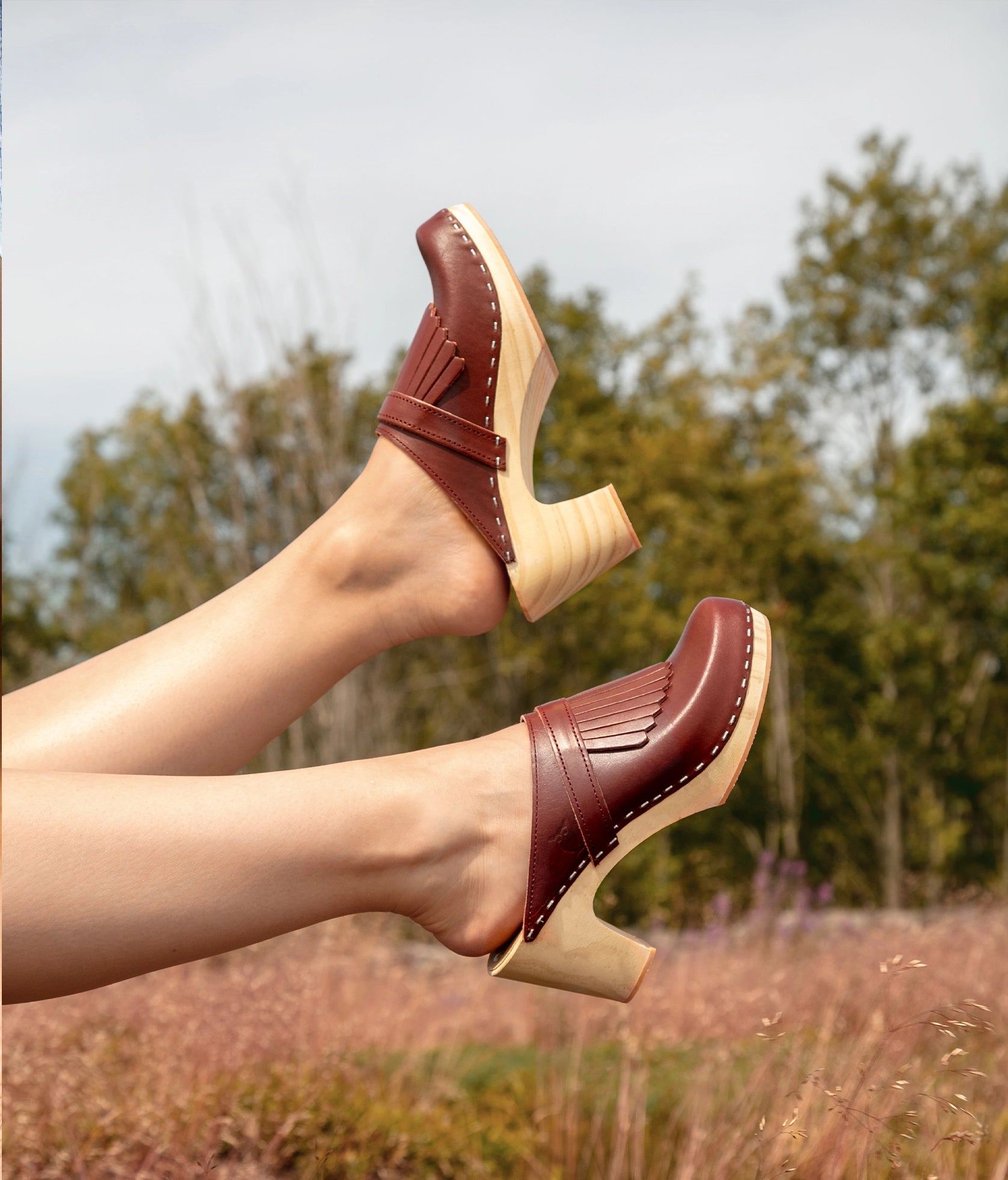 high rise clog mule in cognac red vegetable tanned leather stapled on a light wooden base with a leather strap with fringes