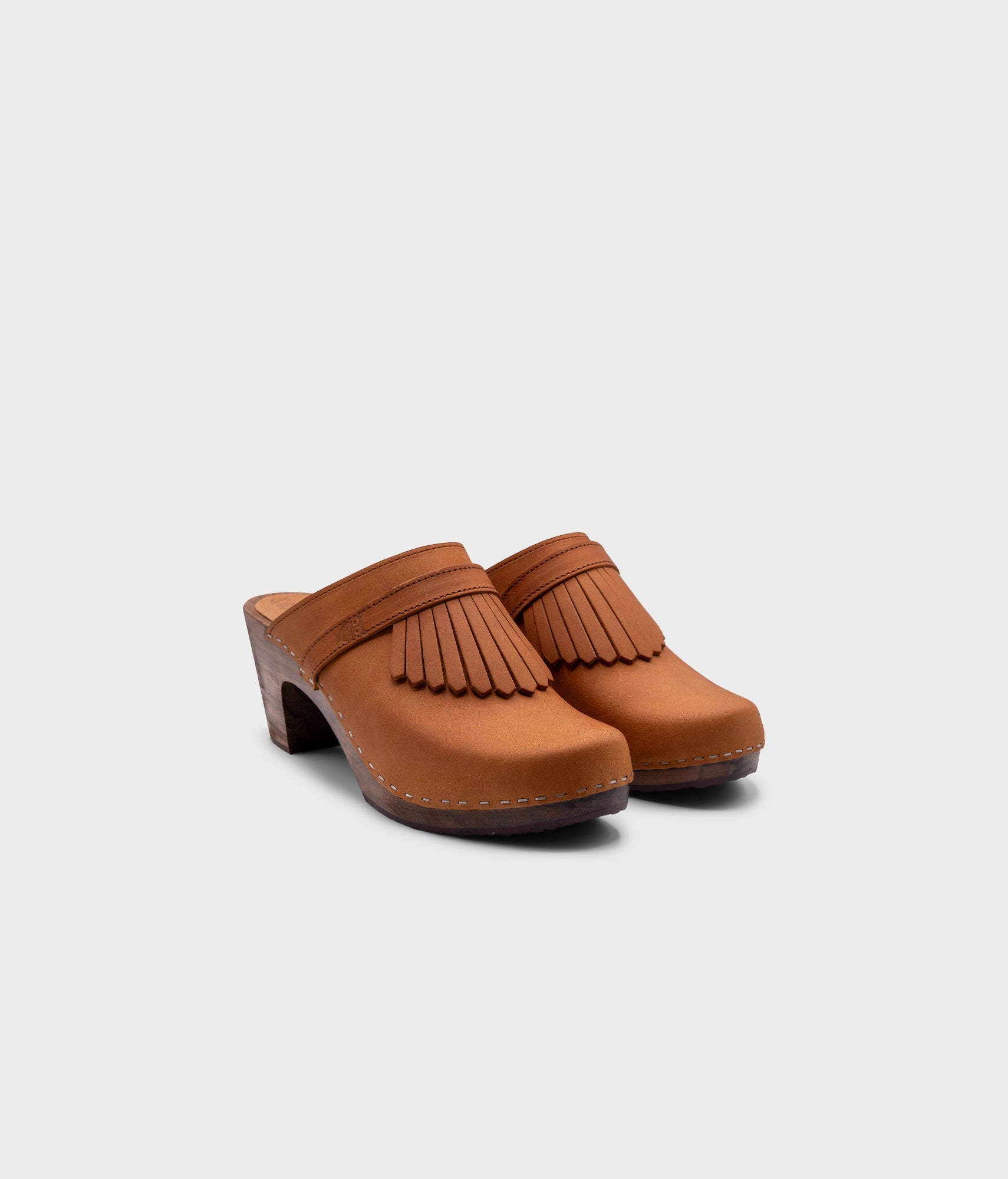 high rise clog mule in light brown nubuck leather stapled on a dark wooden base with a leather strap with fringes