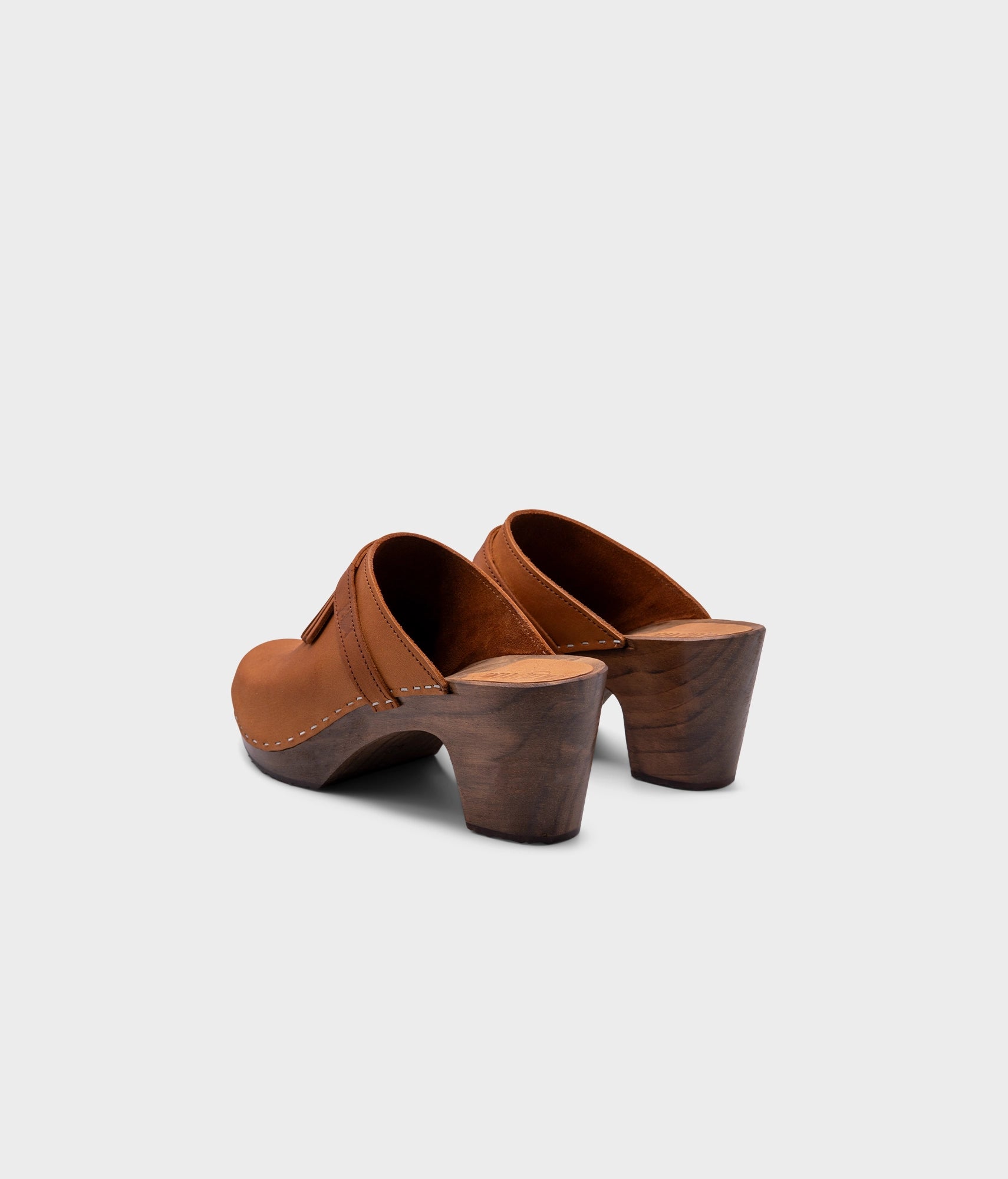 high rise clog mule in light brown nubuck leather stapled on a dark wooden base with a leather strap with fringes