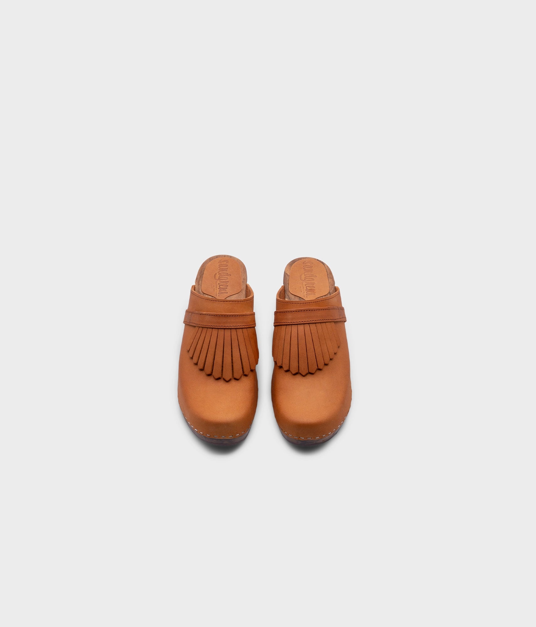 high rise clog mule in light brown nubuck leather stapled on a dark wooden base with a leather strap with fringes