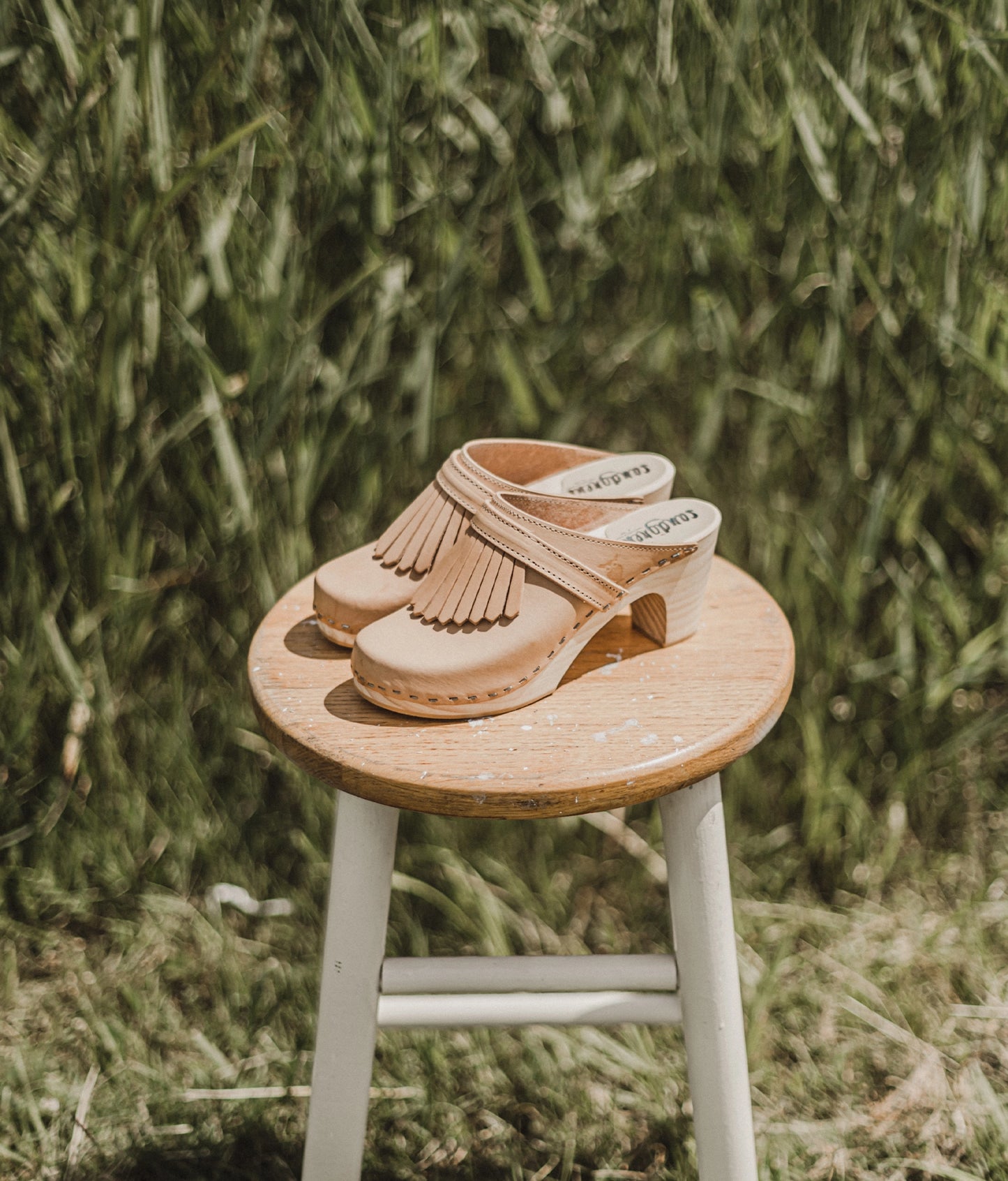 high rise clog mule in ecru beige vegetable tanned leather stapled on a light wooden base with a leather strap with fringes