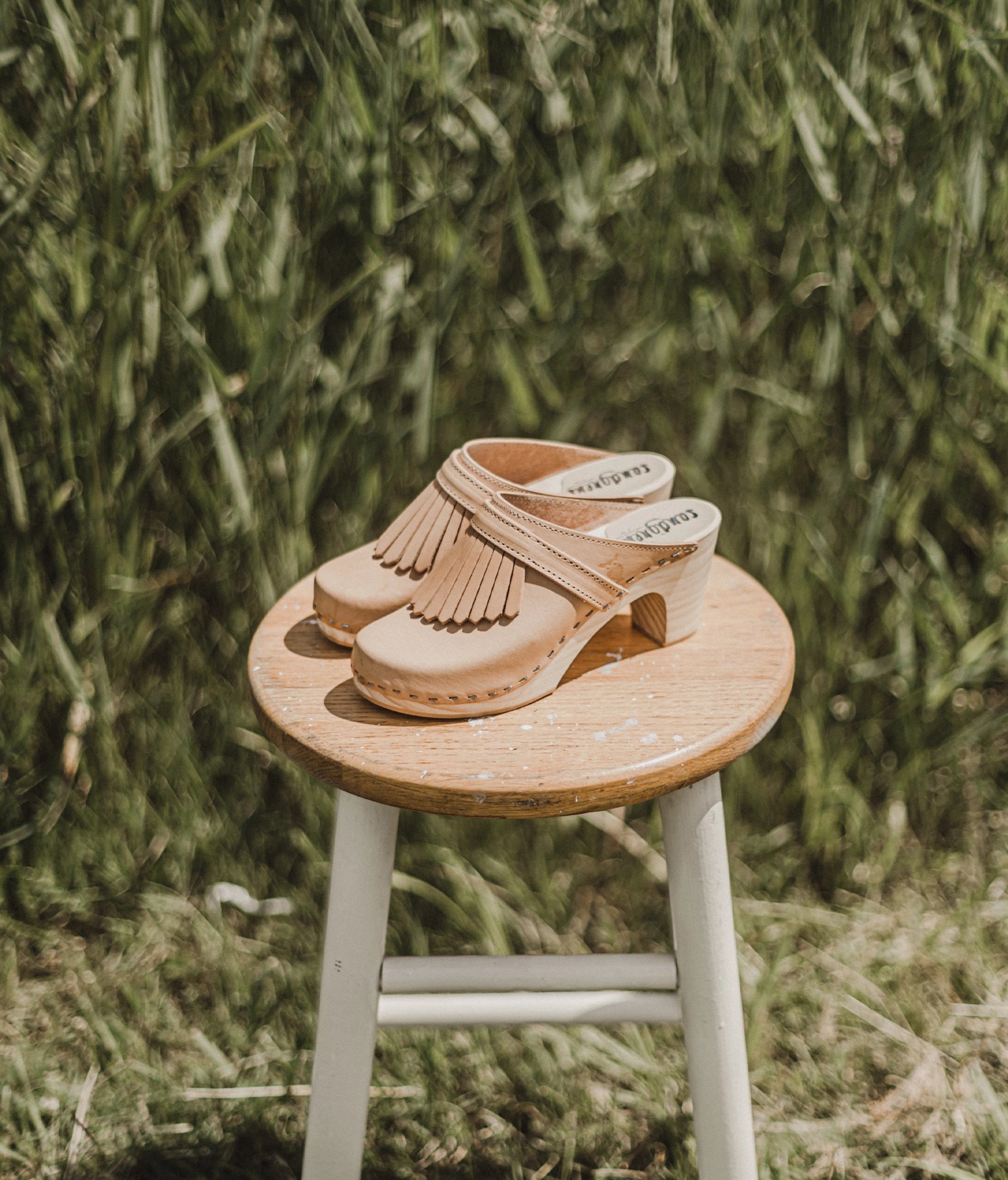 high rise clog mule in ecru beige vegetable tanned leather stapled on a light wooden base with a leather strap with fringes