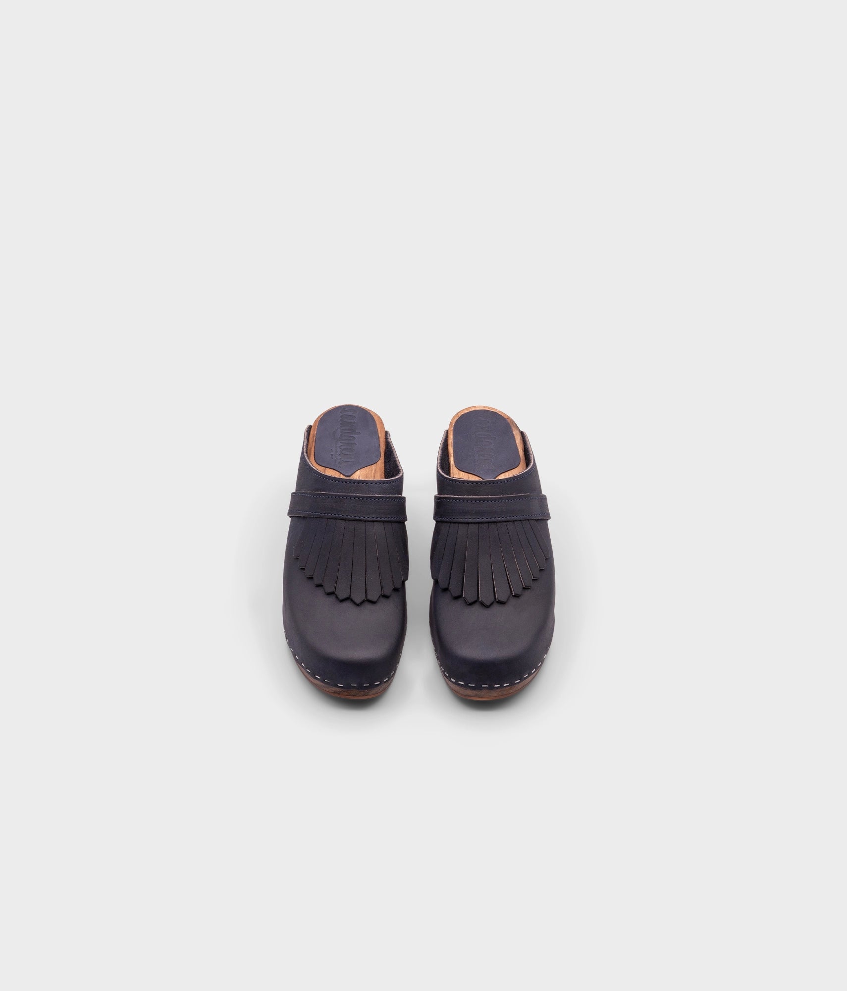 high rise clog mule in navy blue nubuck leather stapled on a dark wooden base with a leather strap with fringes