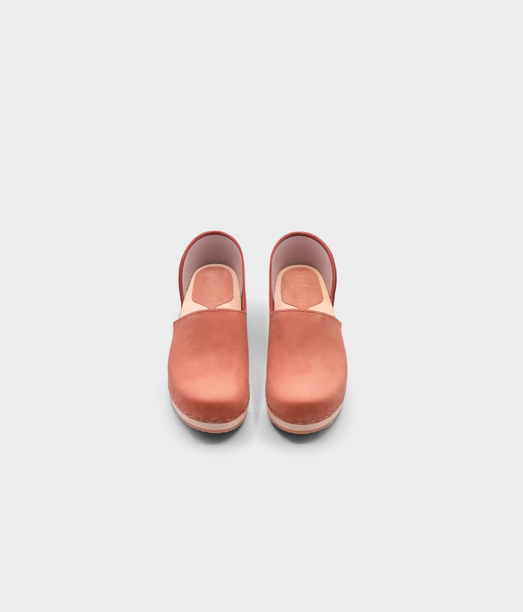 low heeled closed-back clogs in blush pink nubuck leather stapled on a light wooden base